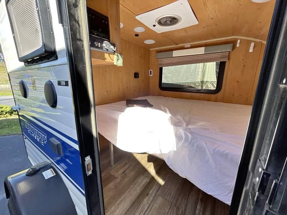 Compact RV rental interior: A cozy bed, small kitchen, and wood paneling in this Sunray Classic camper.. Sunset Park RV SunRay 2019