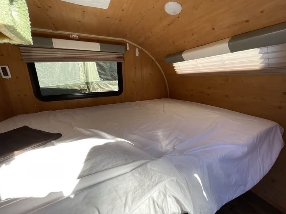 Spacious RV rental bedroom with a comfy bed, wood walls, and windows, perfect for your next adventure.. Sunset Park RV SunRay 2019