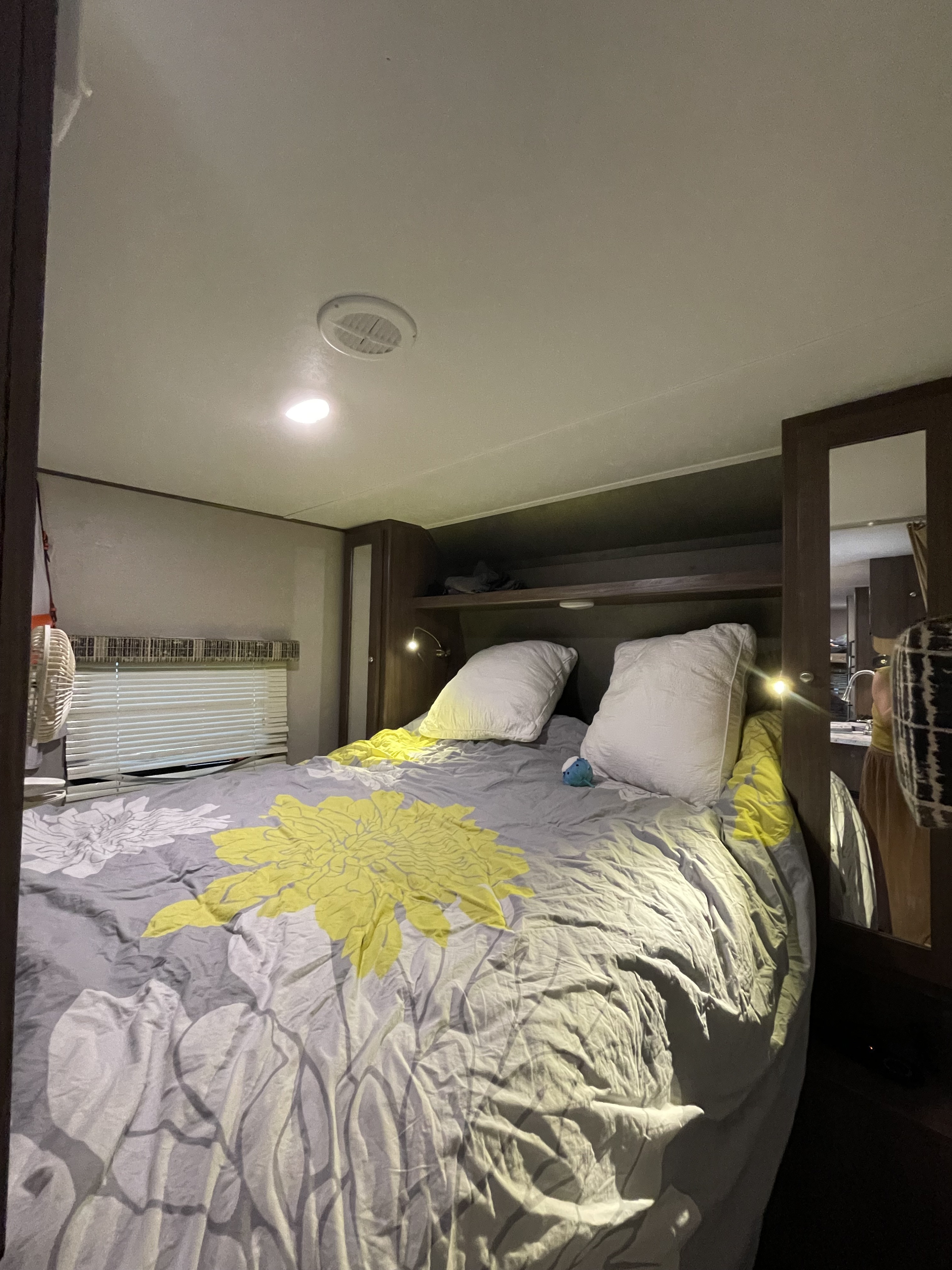 Cozy RV rental bedroom with a floral bedspread, pillows, fan, and built-in storage. Ideal for a comfortable stay.. Keystone RV Hideout 2018
