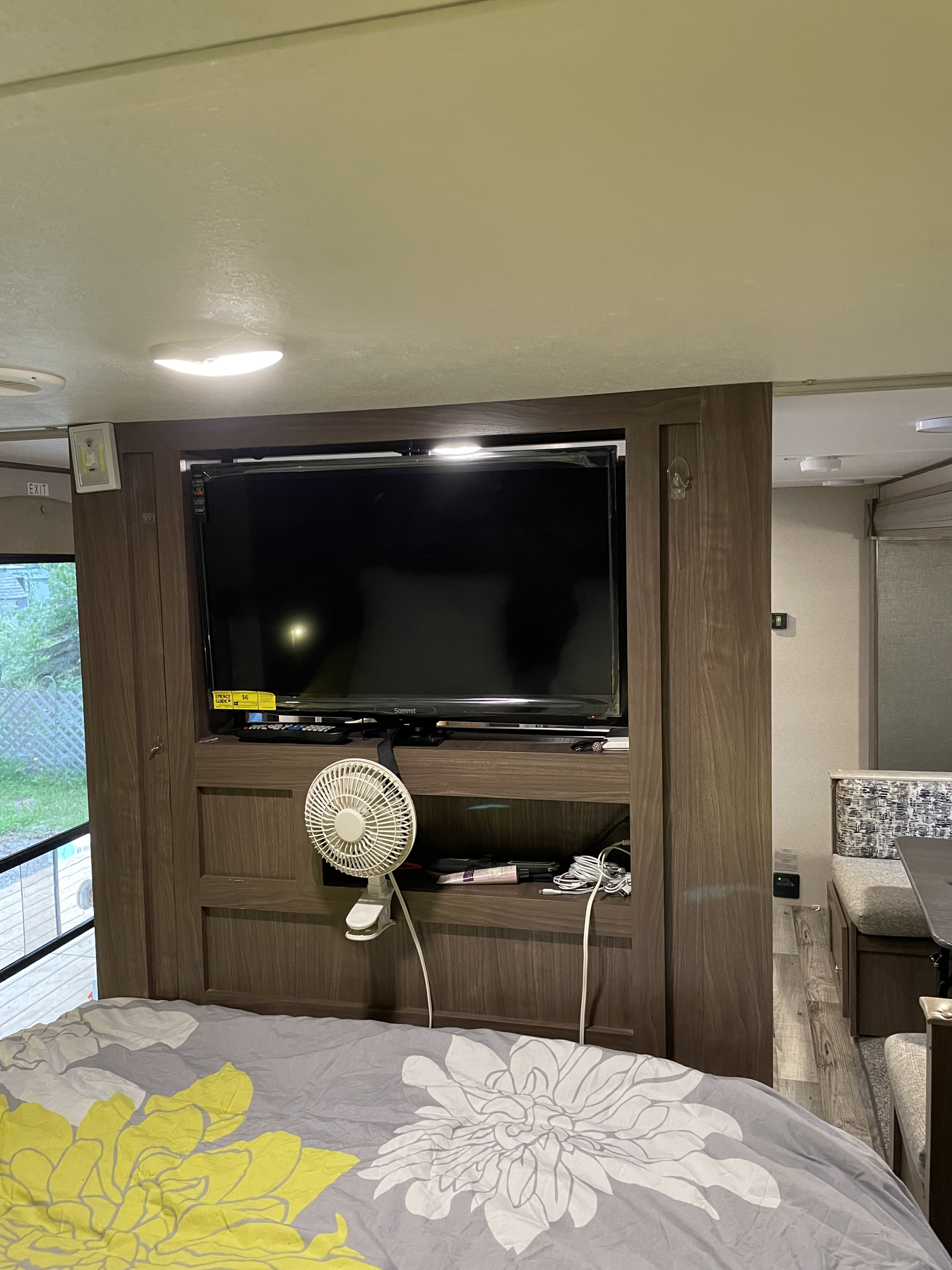 Interior of an RV rental: bedroom with floral duvet, wall-mounted TV, fan, looking into the compact living space.. Keystone RV Hideout 2018