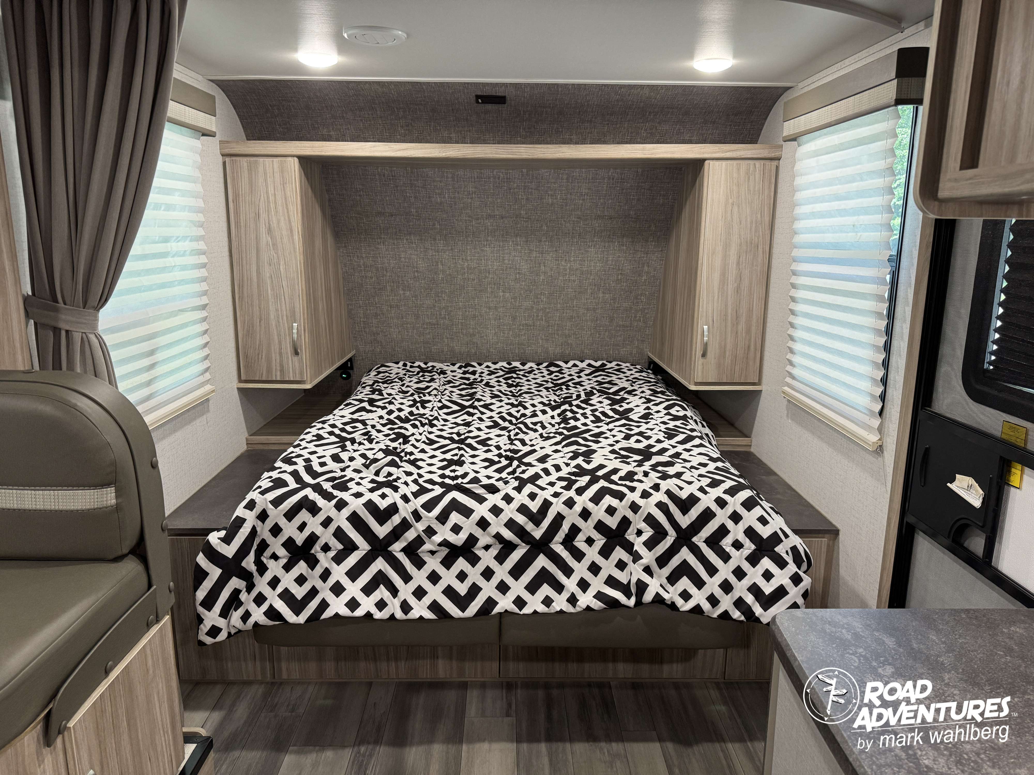 View of a modern RV rental bedroom featuring a bed with a striking black and white comforter and overhead storage.. Winnebago Micro Minnie 2022