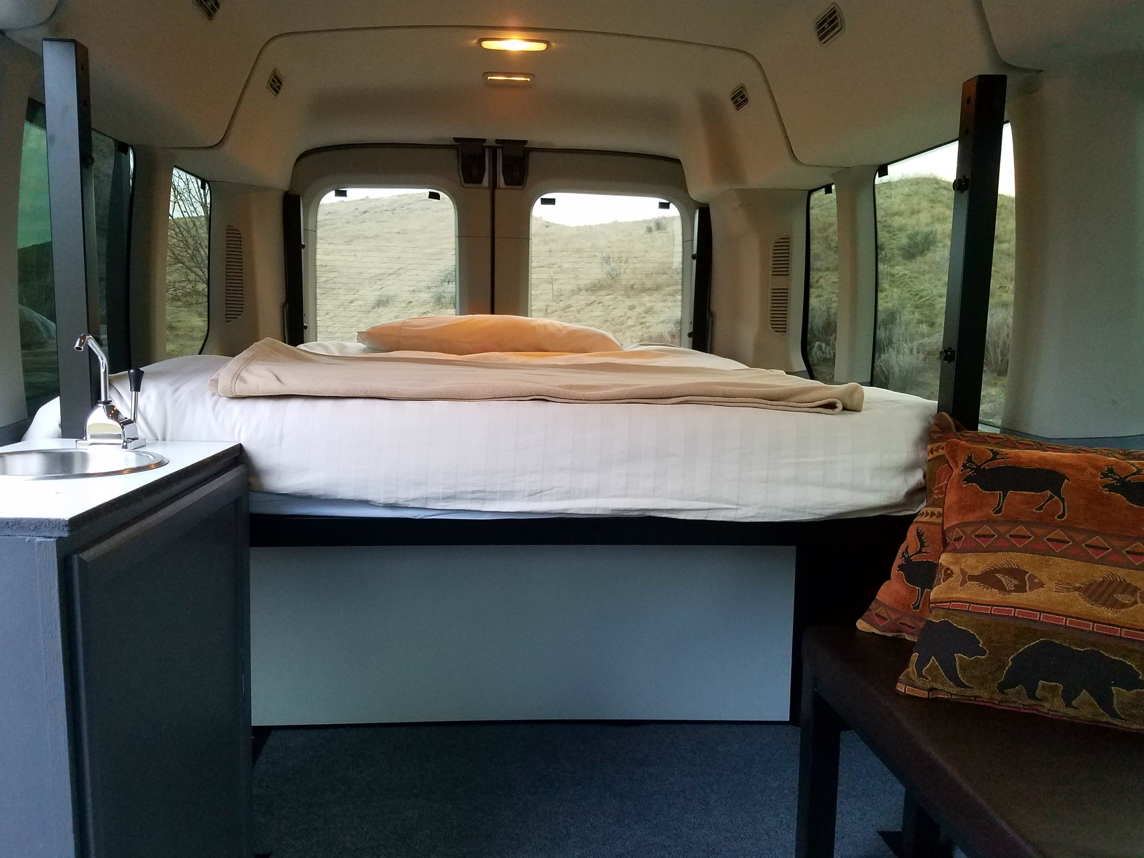 Cozy RV rental interior: comfy bed, functional sink, & scenic views for your next adventure.. Ford Transit 2019