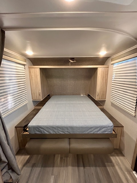 Inside an RV rental, a cozy bedroom featuring a grey mattress, window blinds, and wood cabinetry, ideal for mobile living.. Winnebago Minnie Winnie 2022