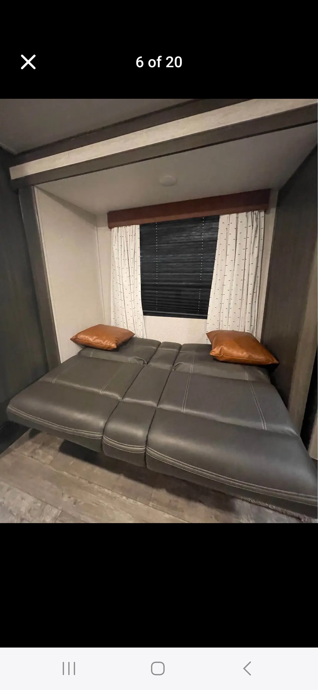 RV rental interior featuring a comfortable dark gray convertible sofa bed with brown pillows, wood-look flooring, and a window with blinds.. forester shasta 2021
