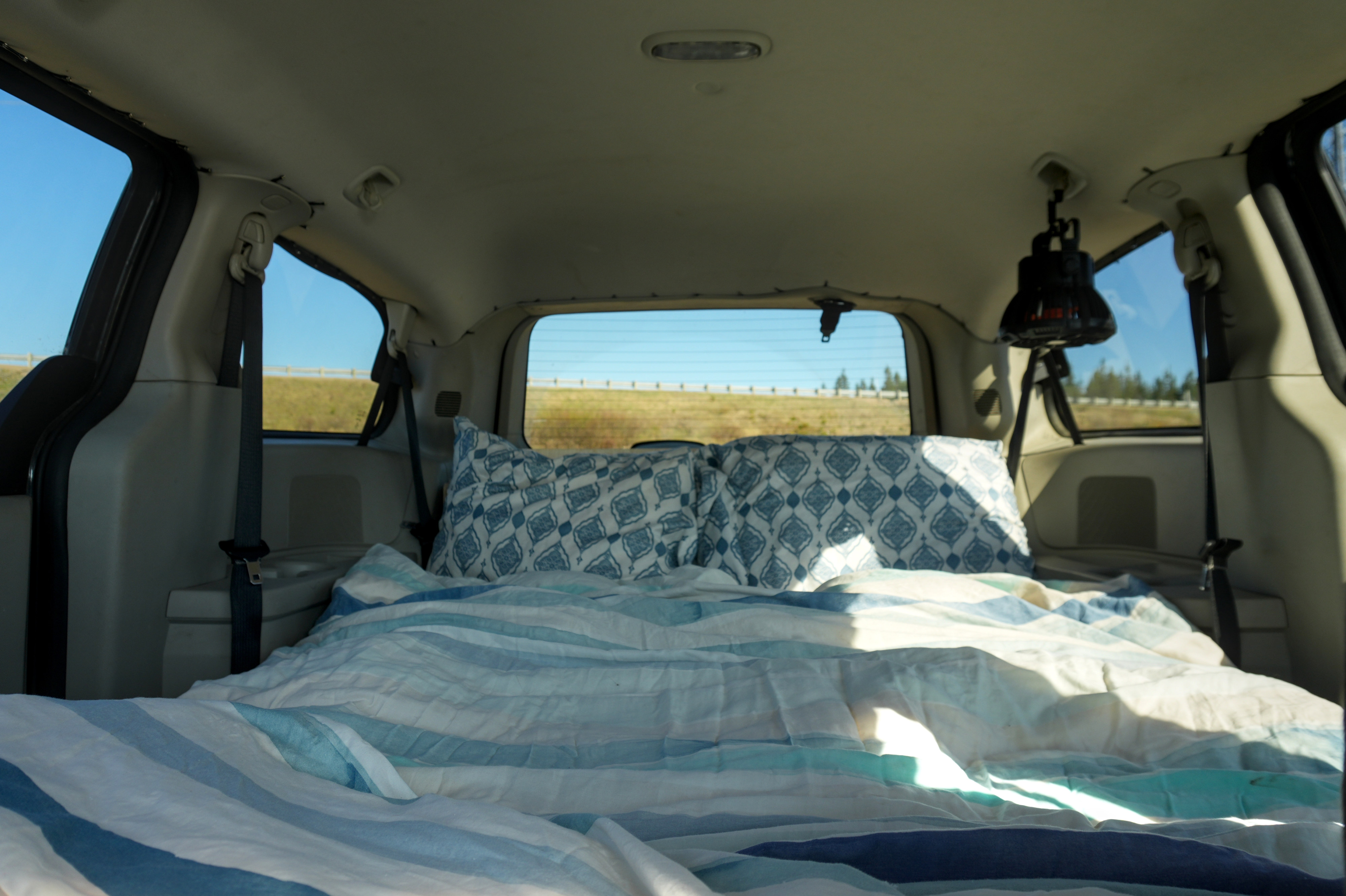 Cozy sleeping setup in a camper van, ideal for your next RV rental adventure. Blue striped bedding and patterned pillows visible.. Dodge Grand Caravan 2013