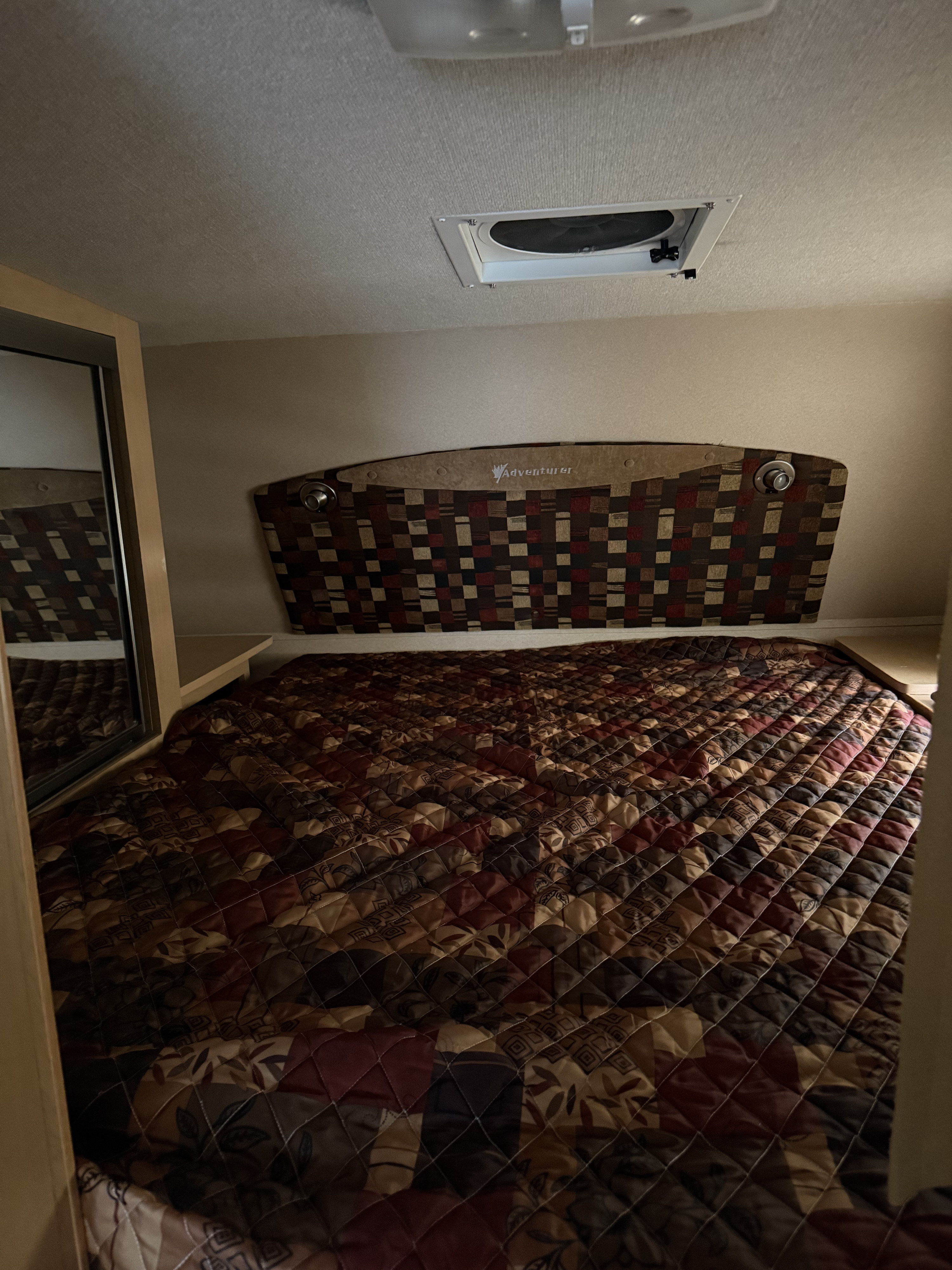 Cozy RV rental bedroom interior featuring a patterned bed, "Adventurer" headboard with lights, and compact layout for travel.. Adventurer Adventurer 2011