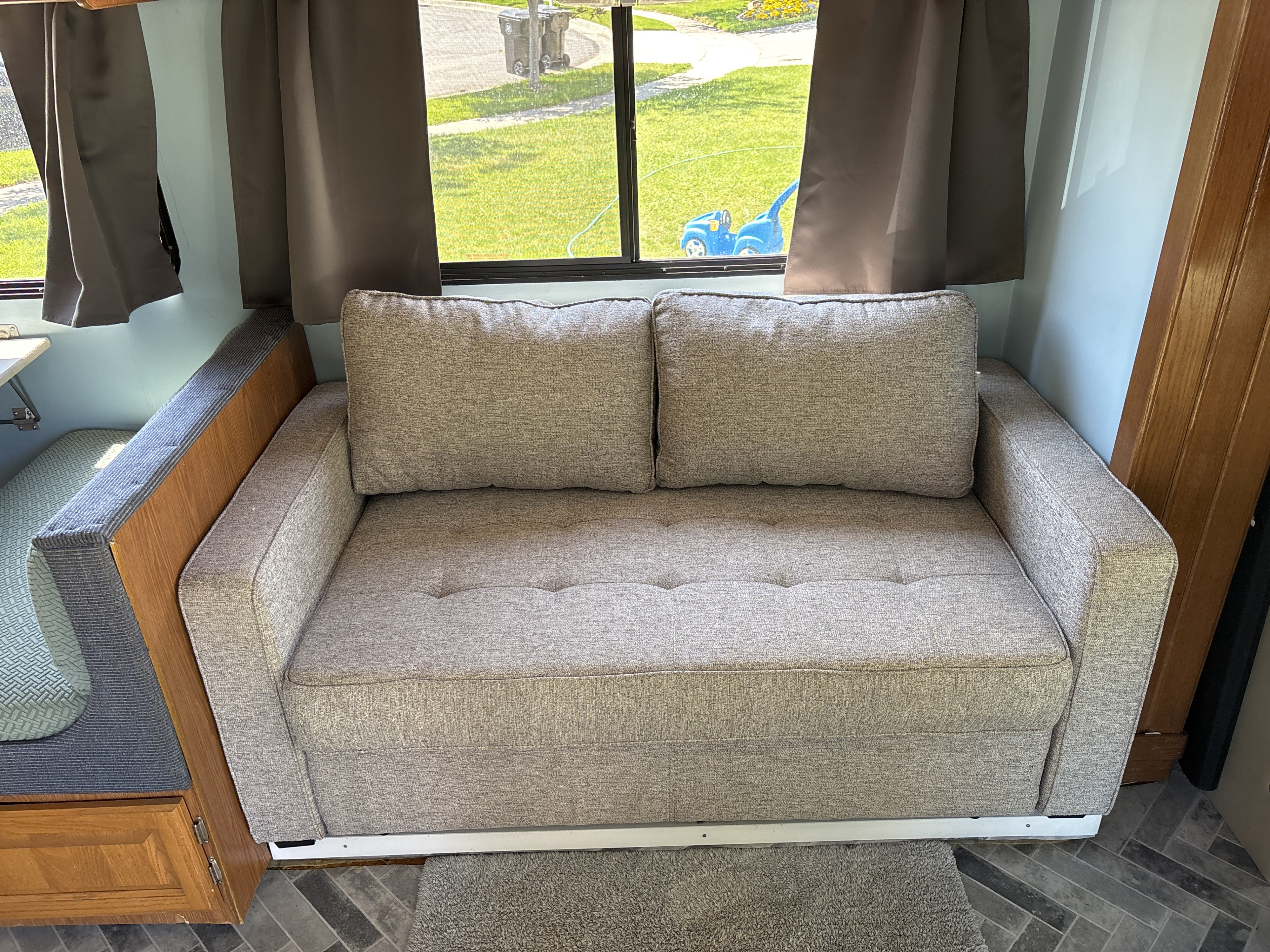 Cozy grey sofa inside an RV rental, with a view of a grassy yard and street through windows.. Four Winds Majestic 2005