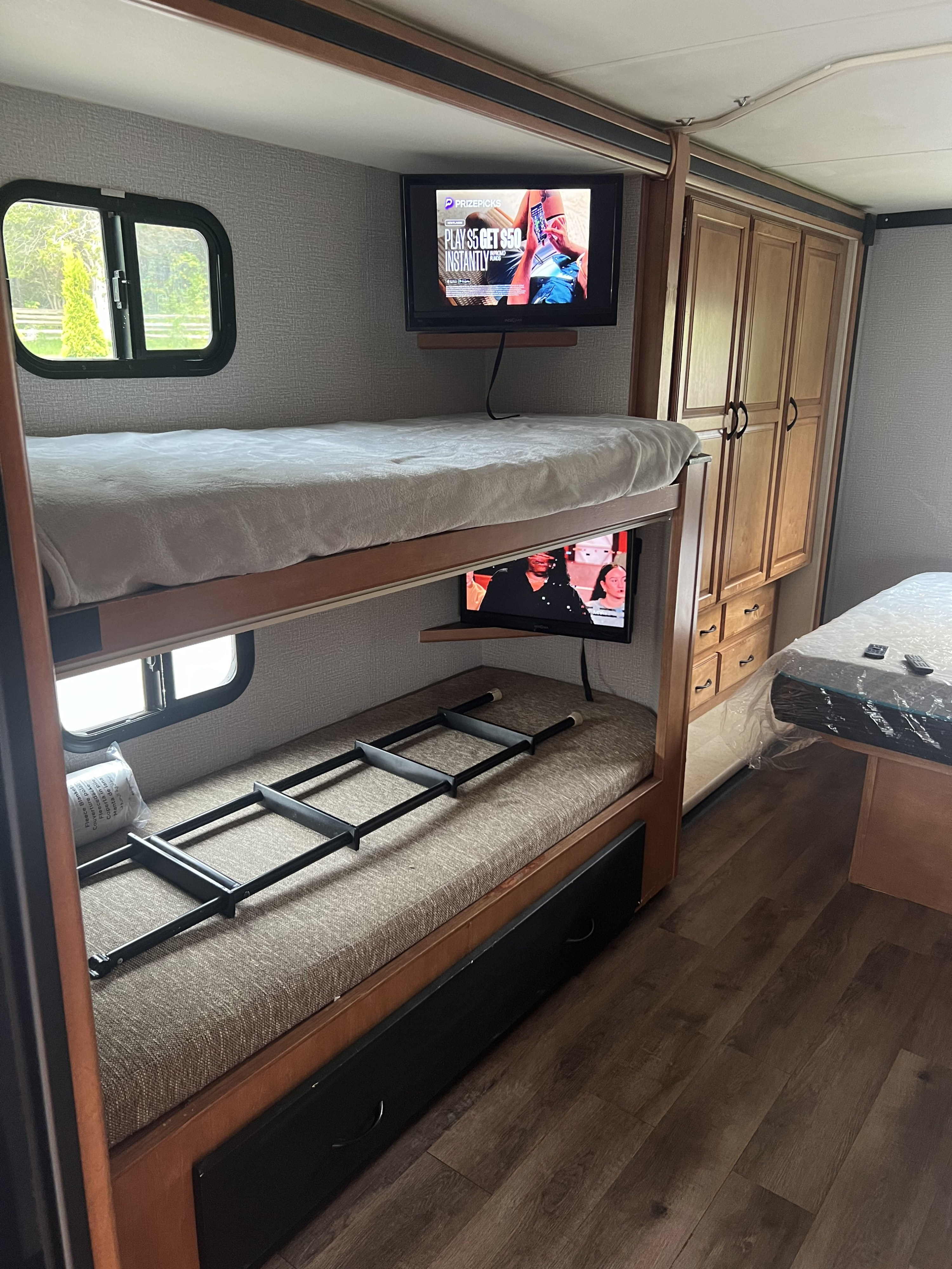 Inside an RV rental, featuring a bunk bed setup with individual TVs, a ladder, and built-in storage on the right.. Winnebago Minnie Winnie 2015