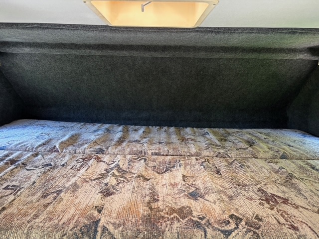 Overhead sleeping area in an RV rental, featuring a patterned bed, soft grey walls, and integrated lighting.. Ford Econoline 1999