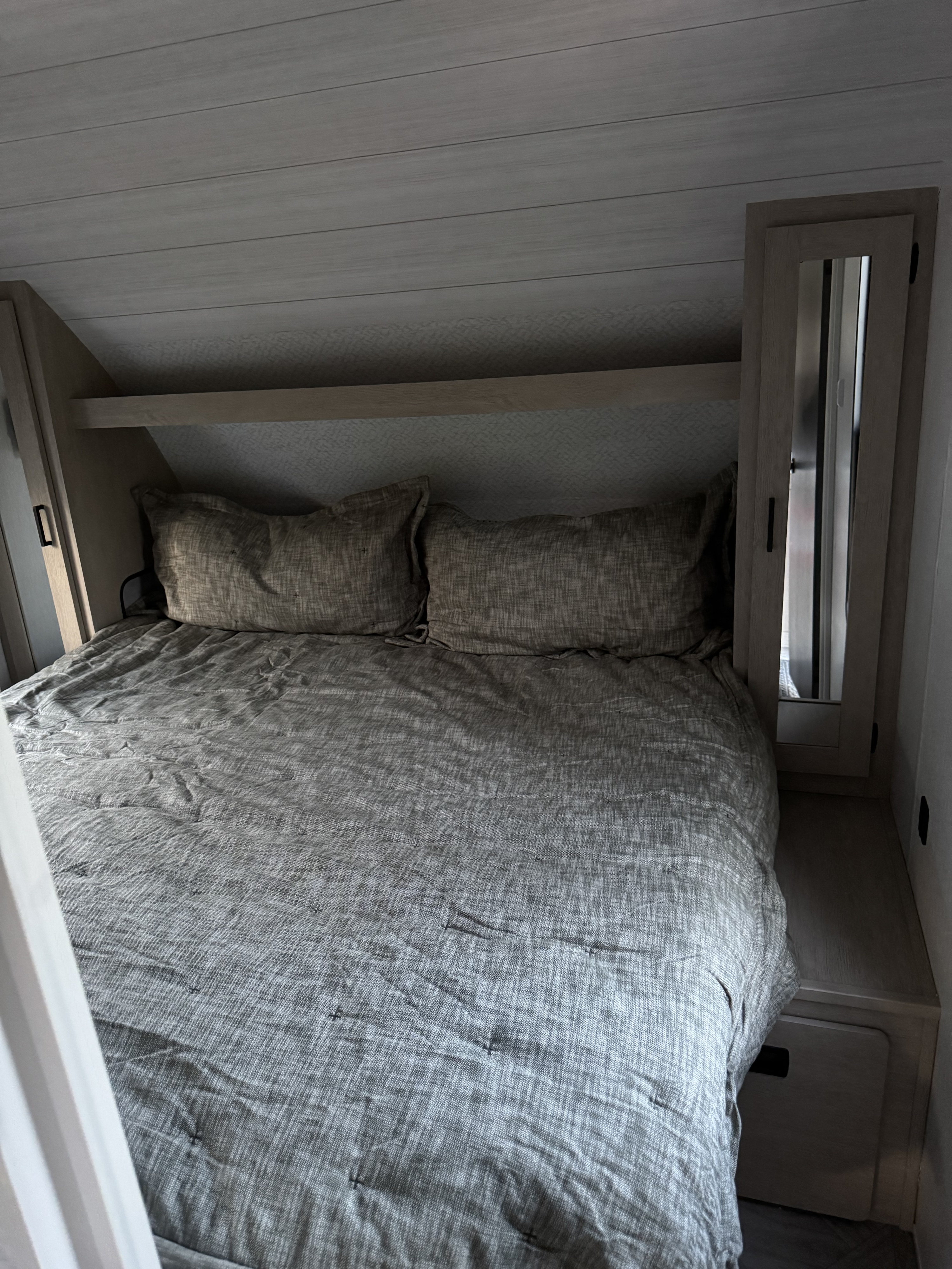 RV rental bedroom with grey bedding, built-in shelves & mirrored cabinet. A compact, cozy sleeping space.. Forest River Wildwood X-Lite 2023