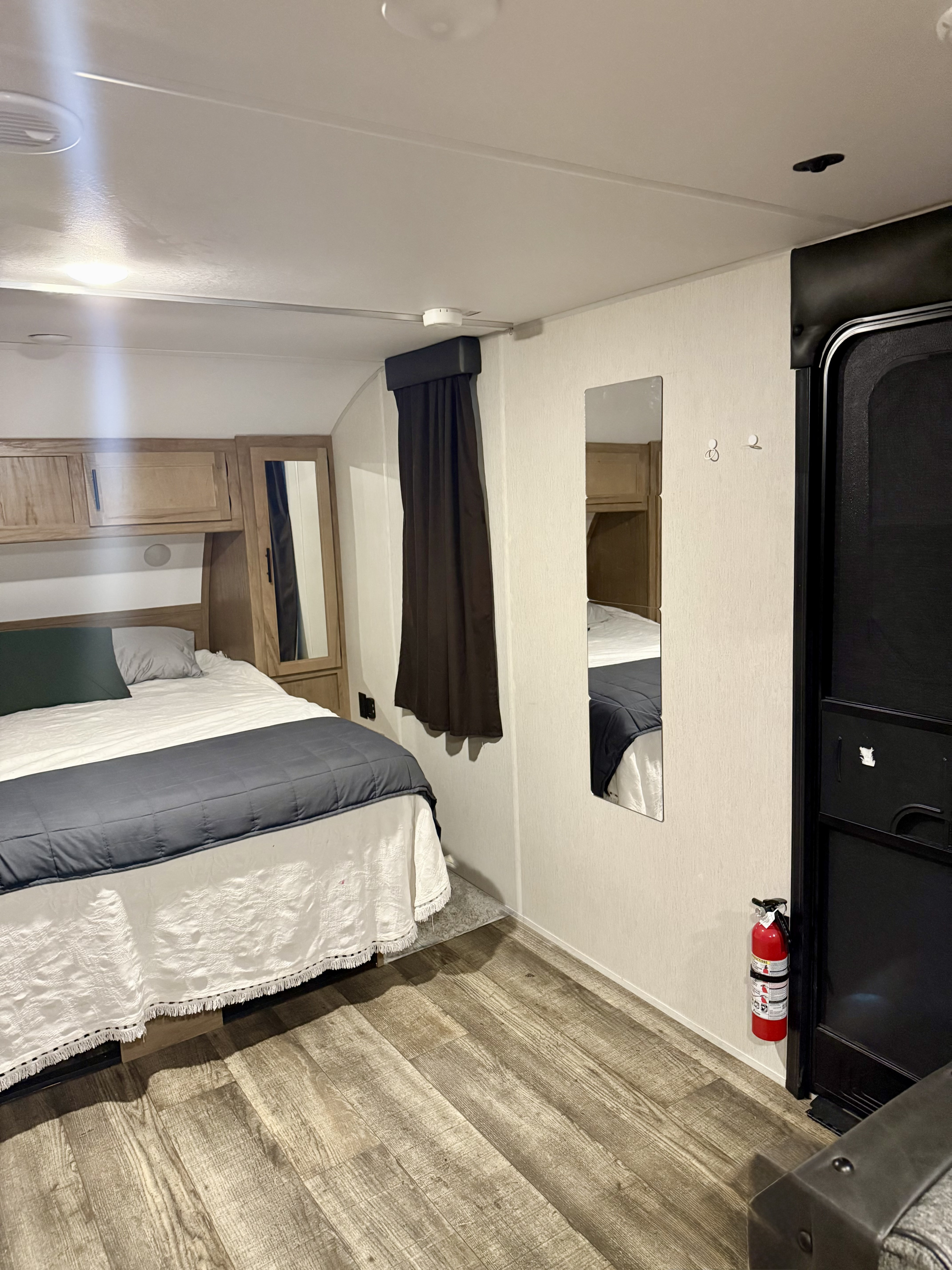 Inside an RV rental bedroom: cozy bed with storage, wood-look floor, wall mirrors, and fire extinguisher for safety.. Forest River Cherokee Grey Wolf Black Label 2023