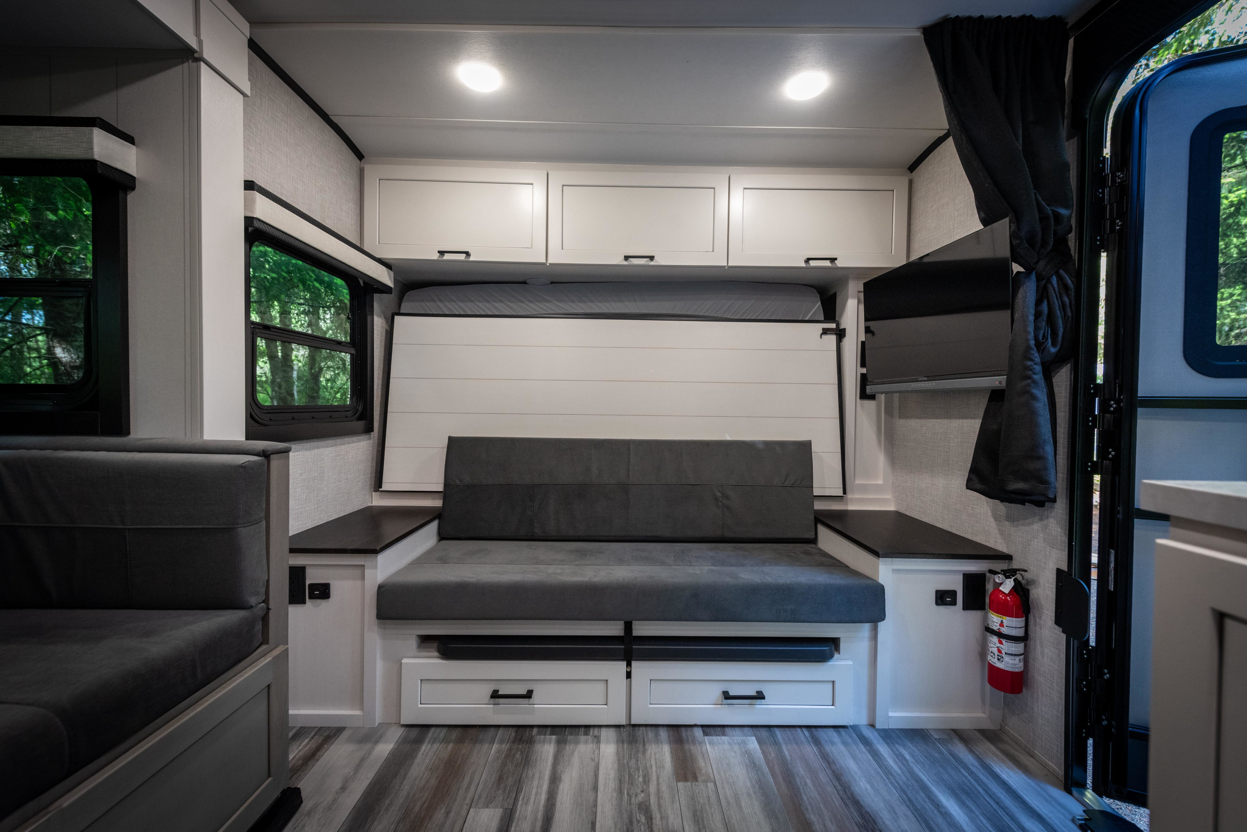 Modern & spacious RV rental interior: grey convertible sofa, pull-down bed, overhead storage, and TV for travel.. Jayco Jay Feather 2025