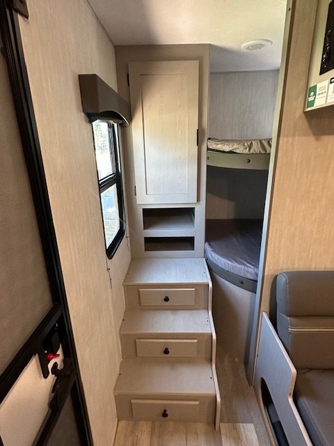 Light-colored RV rental interior featuring storage steps, a cabinet, window, and bunk beds. Perfect for camper trips.. Forest River Forest River Viking 2025