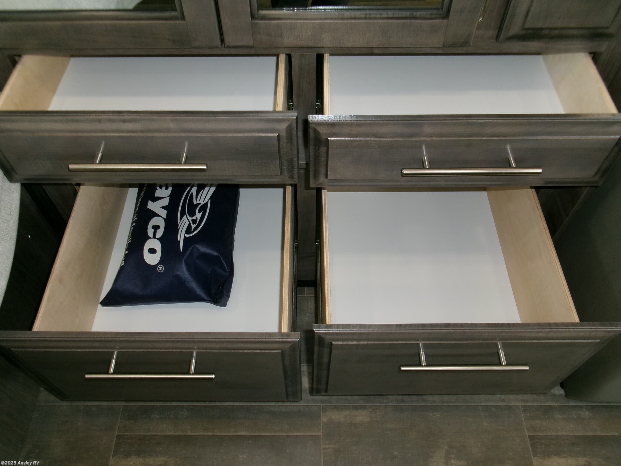 RV rental storage: Four open dark wood drawers with white liners, one holding a blue bag, offer organized RV interior storage.. Jayco Melbourne 2023