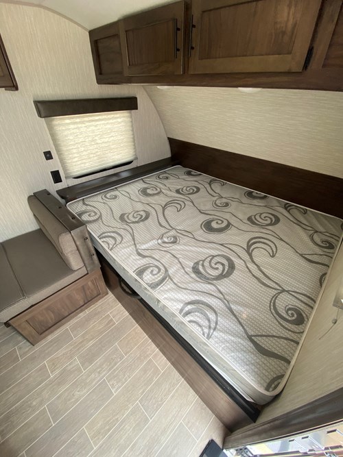 Cozy RV rental interior featuring a bed with patterned mattress, overhead cabinets, window, and small bench seating.. Cherokee Wolf Pup 2021