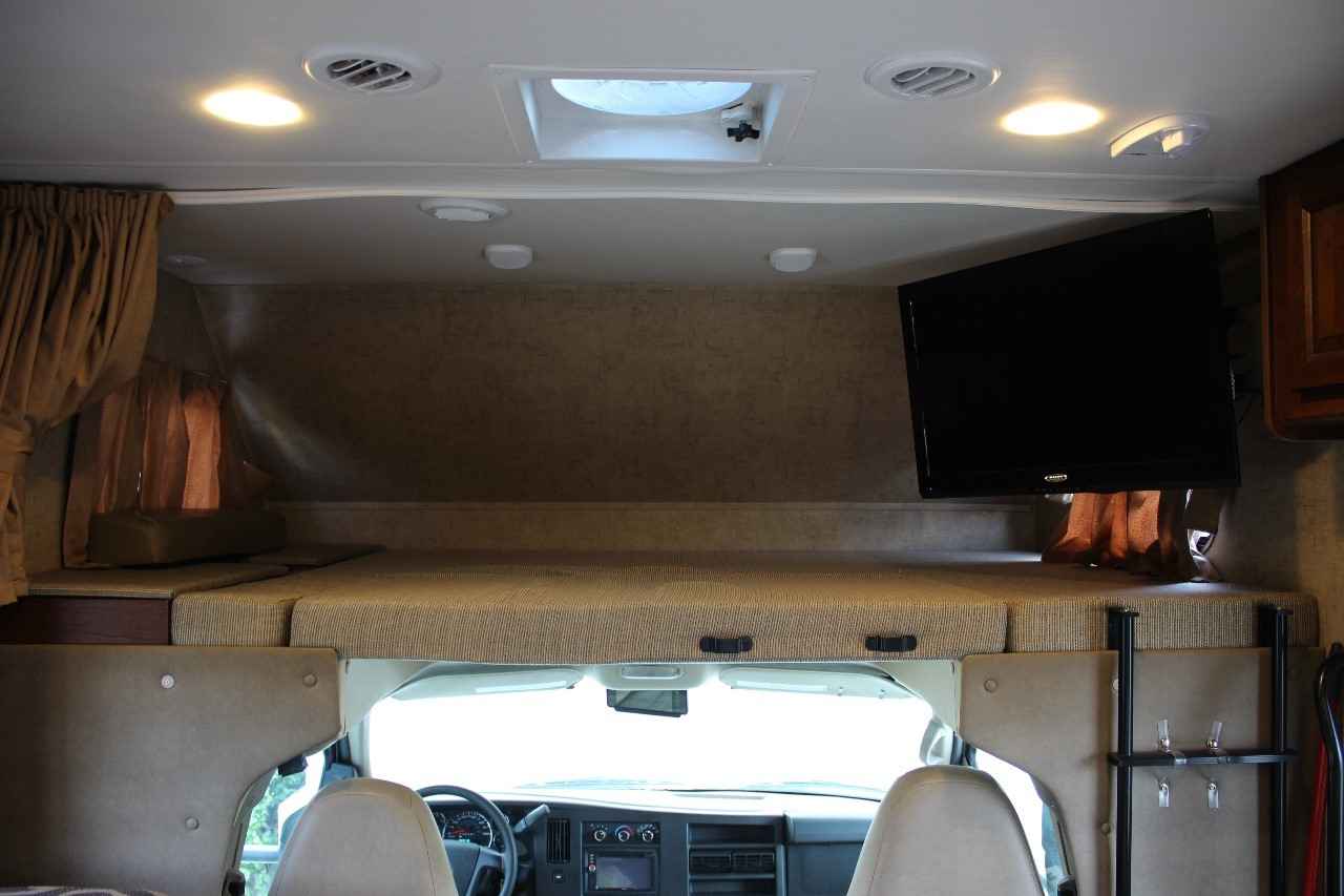 Inside an RV rental: View of the cab-over bunk with a TV and mattress, looking down into the driver's cockpit area.. Forest River Forester 2015