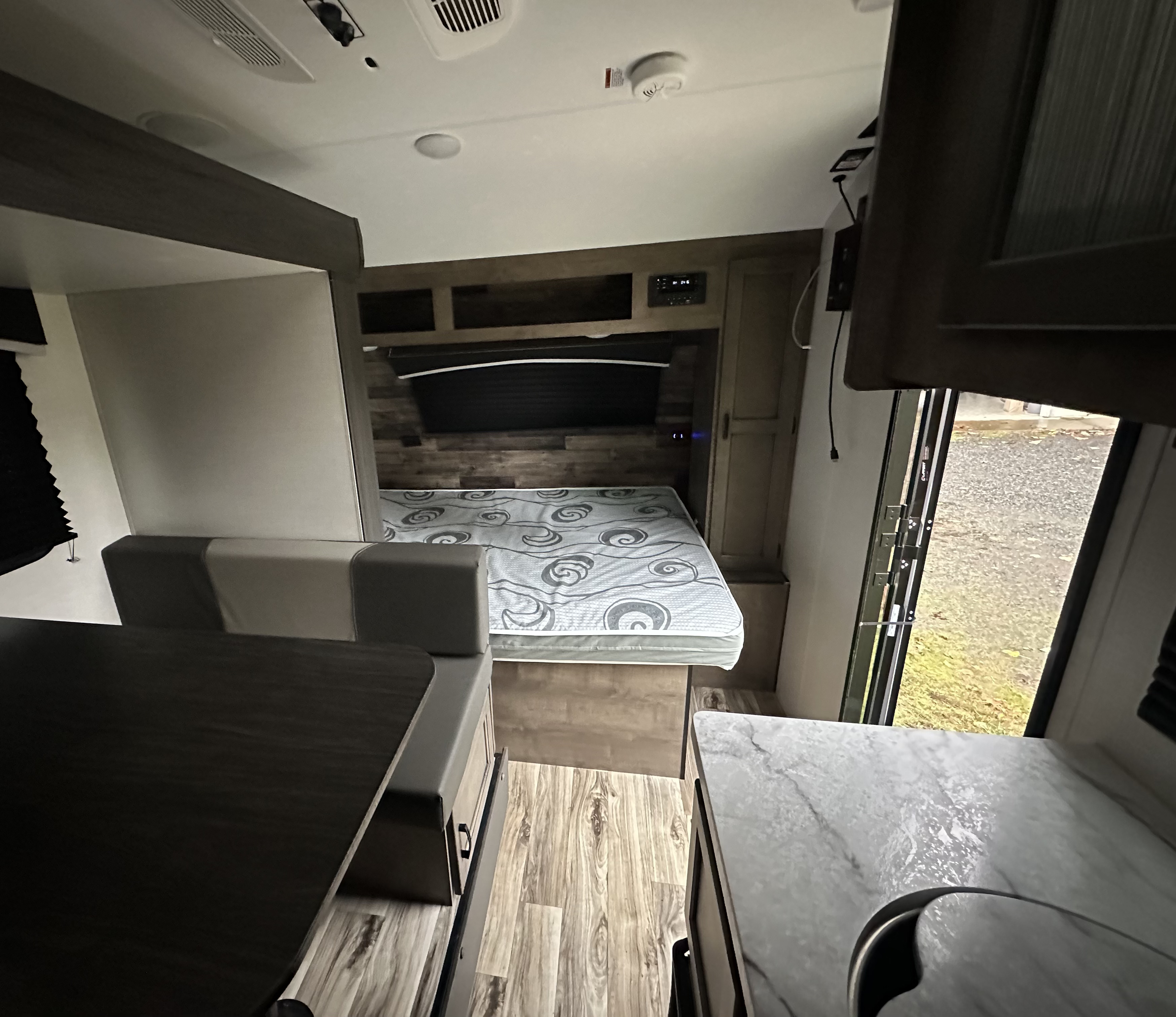 RV rental interior with a cozy bedroom, dinette seating, and compact kitchen. Features modern finishes and wood-look flooring.. Venture RV SL169VUD 2023
