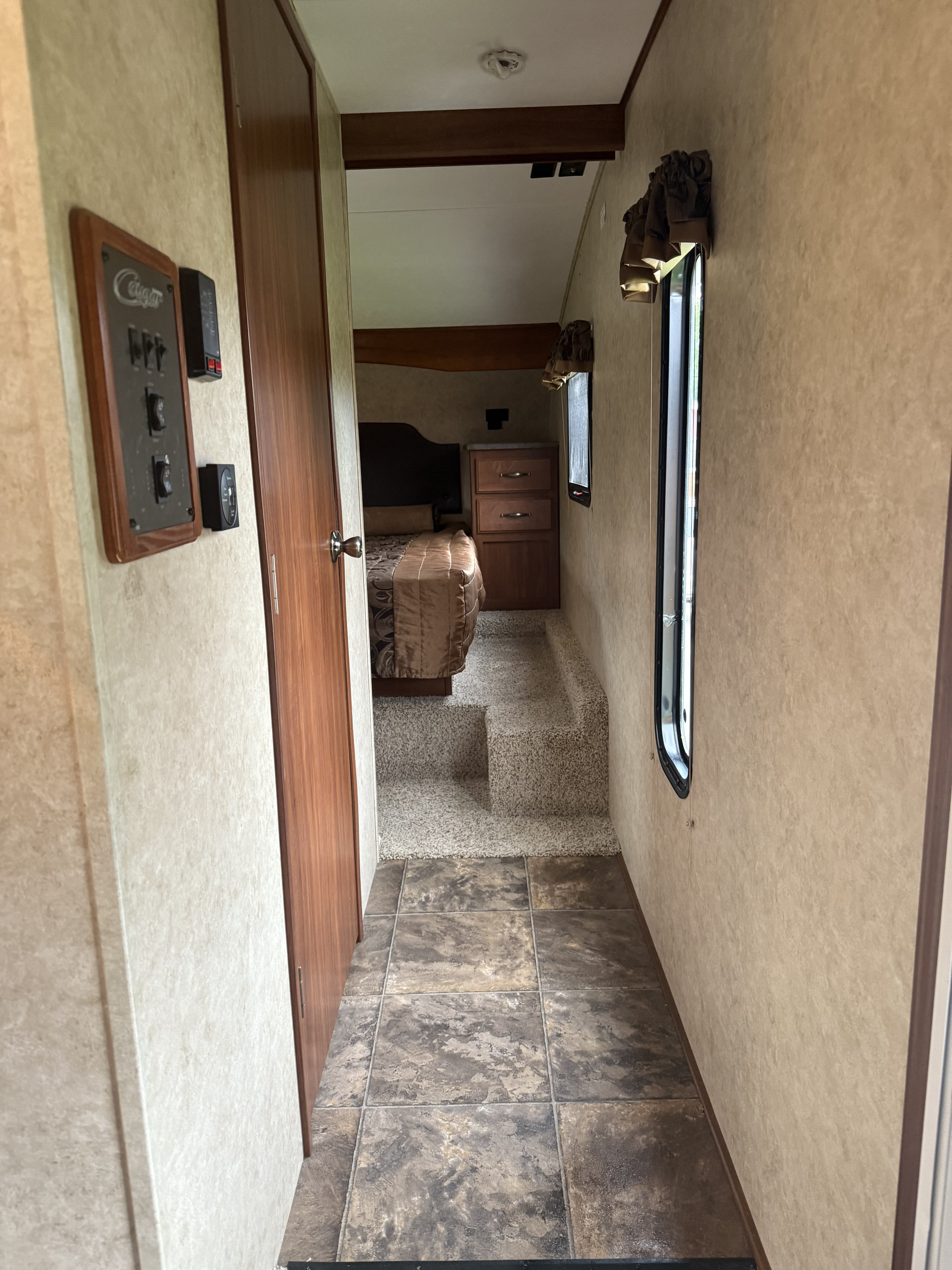 RV rental: Tiled hallway with controls leading to carpeted steps up to an elevated bedroom with a bed and dresser.. Keystone RV Cougar 2015