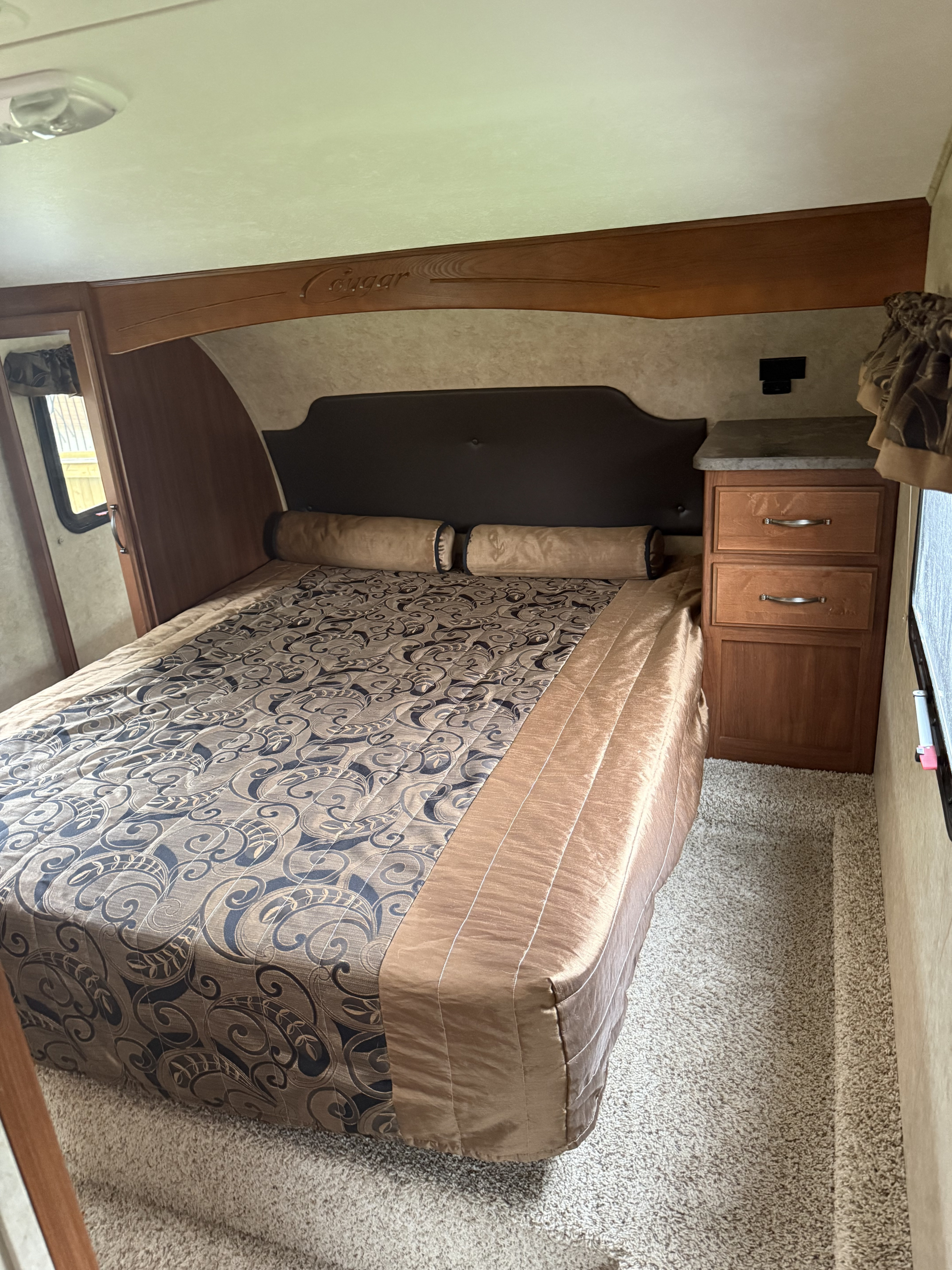 Comfortable Cougar RV rental bedroom featuring a spacious bed with patterned bedding, nightstand, and ample light.. Keystone RV Cougar 2015