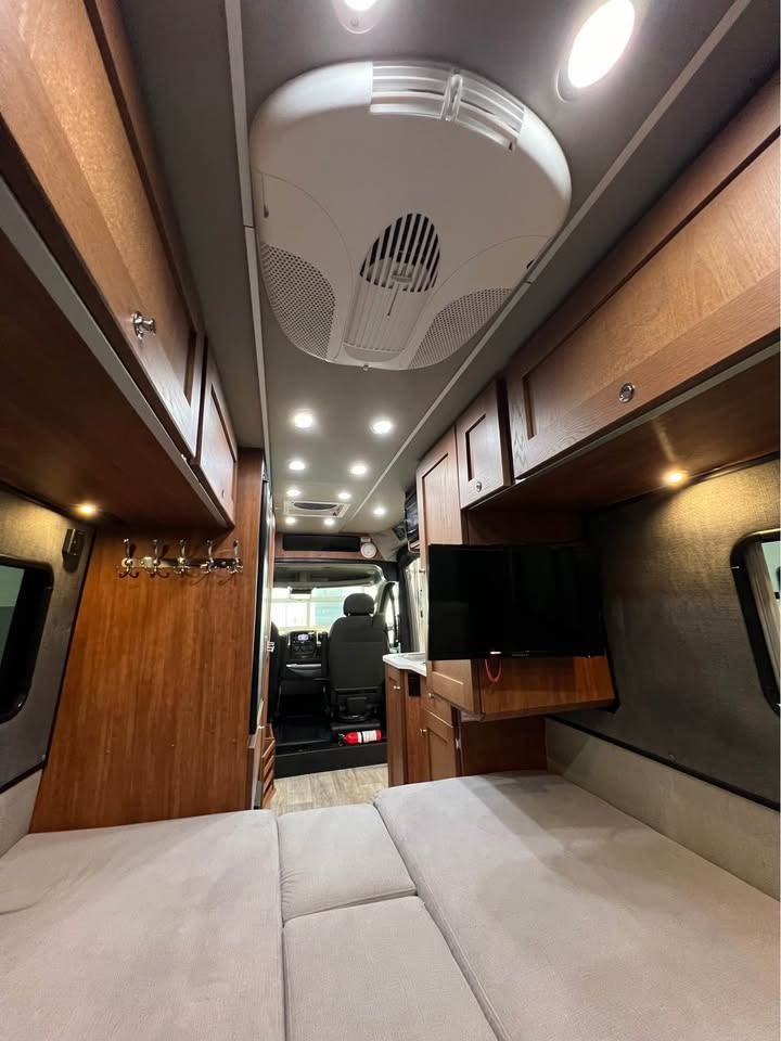 Spacious rv rental interior showing a comfortable bed, overhead AC, wall-mounted TV, and wooden cabinetry.. Roadtrek Roadtrek Class B 2021
