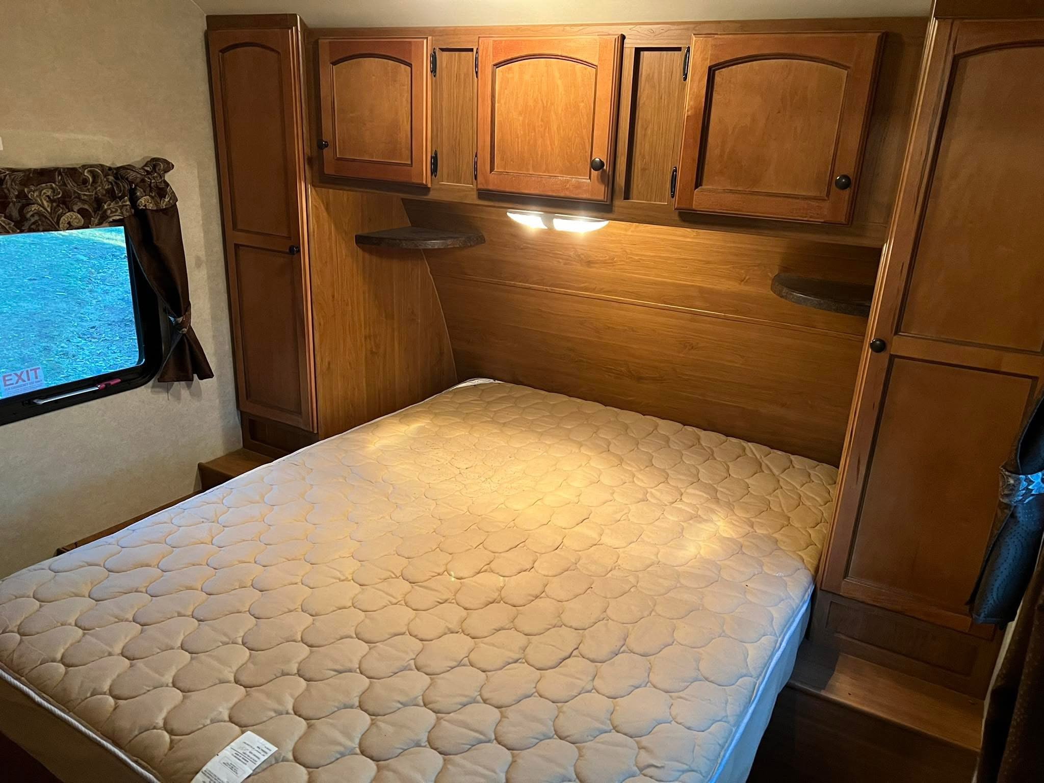 Comfortable RV bedroom featuring a quilted mattress, wooden overhead cabinets, side storage, and a window in this RV rental.. Crossroads RV Sunset Trail 2012