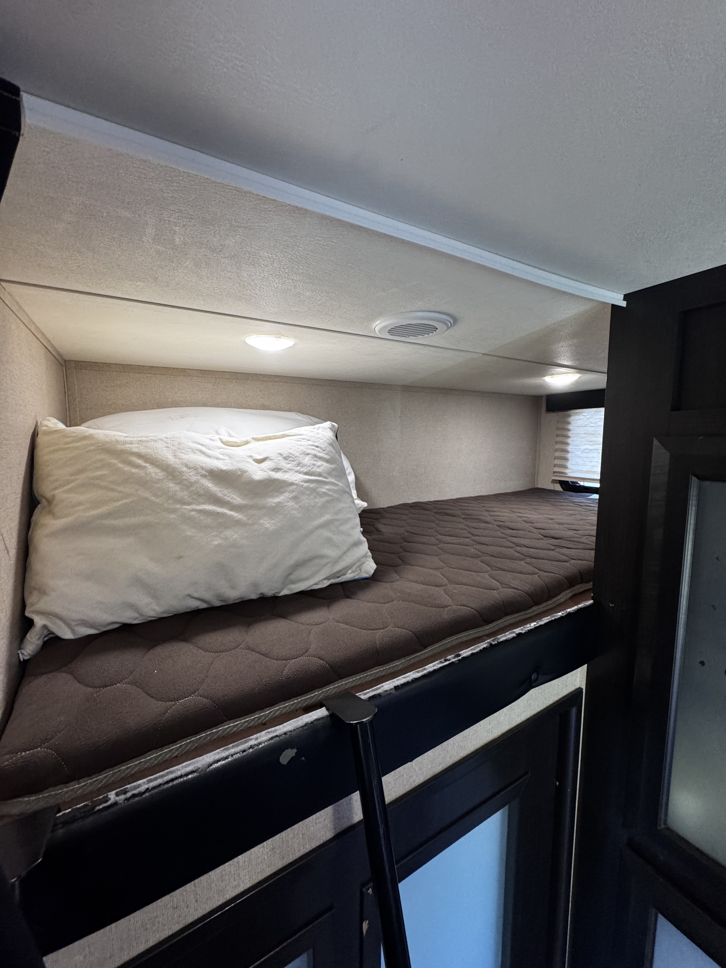 Upper bunk bed in an RV rental, featuring a comfortable mattress, pillow, and ceiling lights, ideal for sleeping on the go.. Dutchmen Voltage 2018