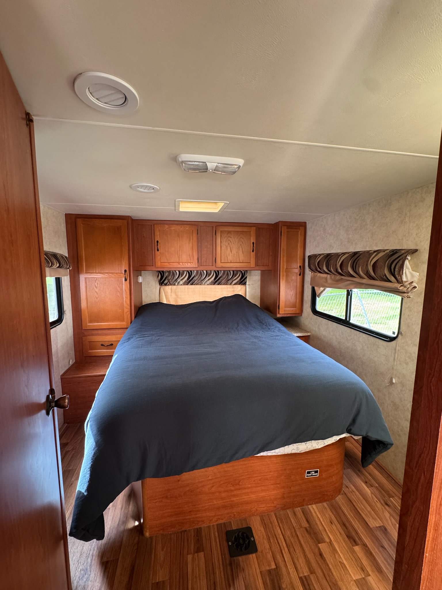 Comfortable RV rental bedroom featuring a large bed, warm wood cabinetry, laminate flooring, and natural light.. Coachmen Freelander 2014