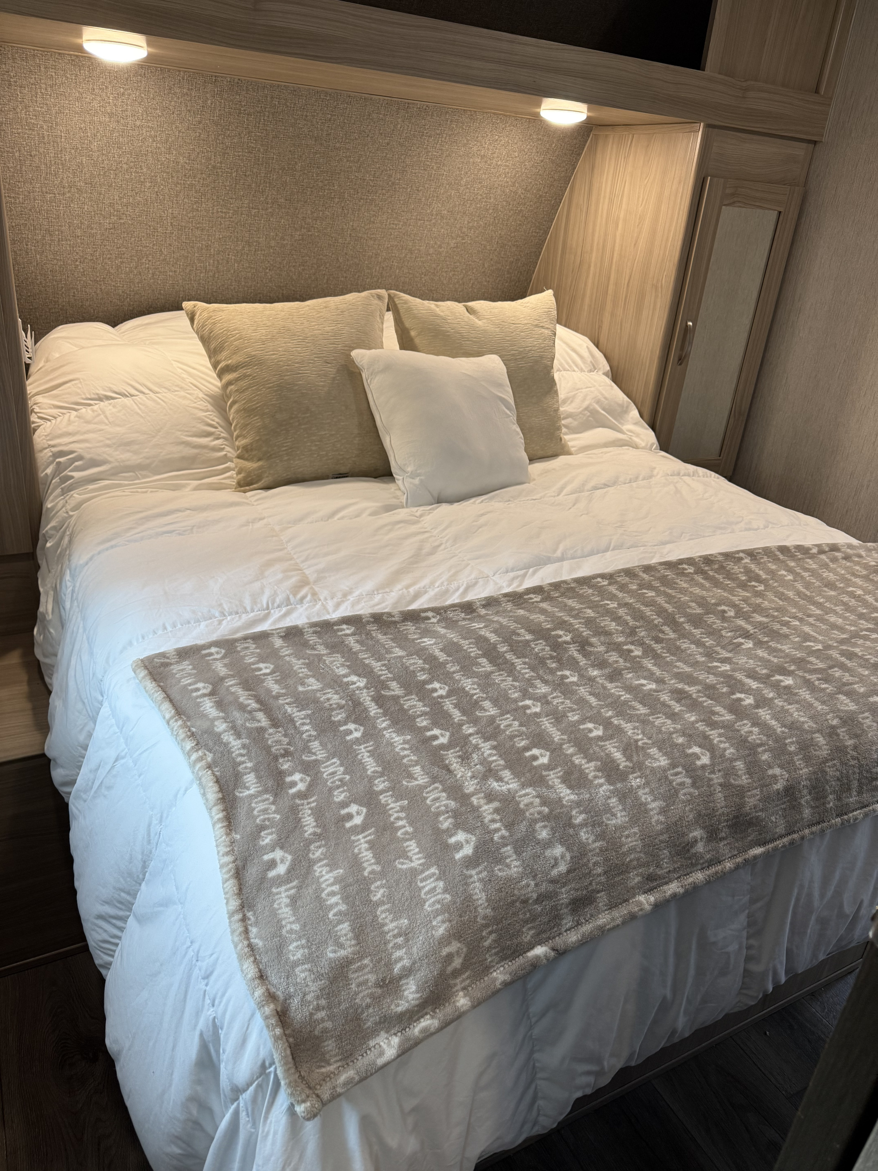 Inside an RV rental: a neatly made bedroom featuring a comfortable bed, throw pillows, and a unique dog-themed blanket.. Coachmen Freedom Express Select 2021