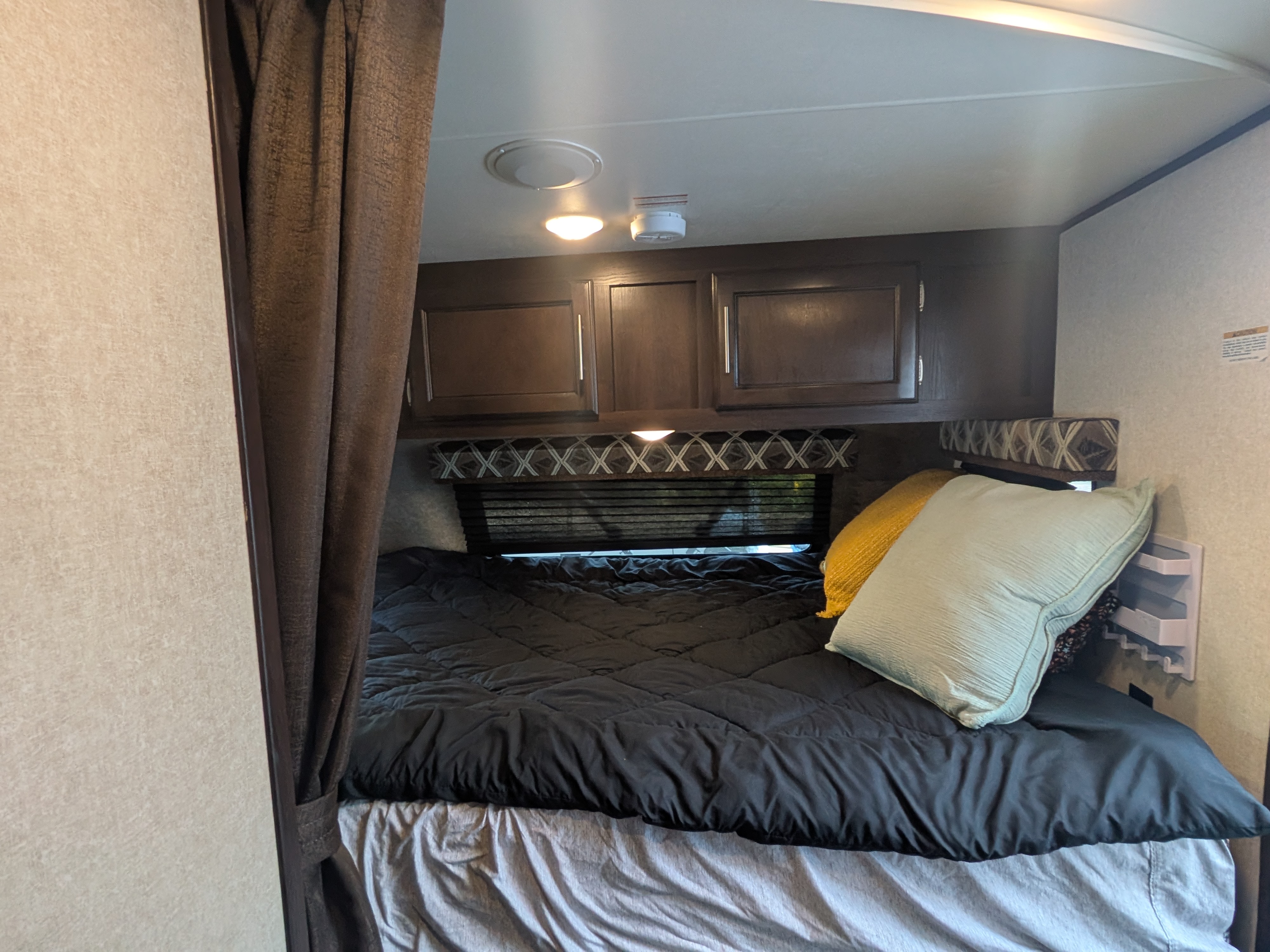 Experience comfort in this RV rental bedroom, featuring a cozy bed, overhead cabinets, and a window. Perfect for your next adventure.. Jayco Jay Flight 2019