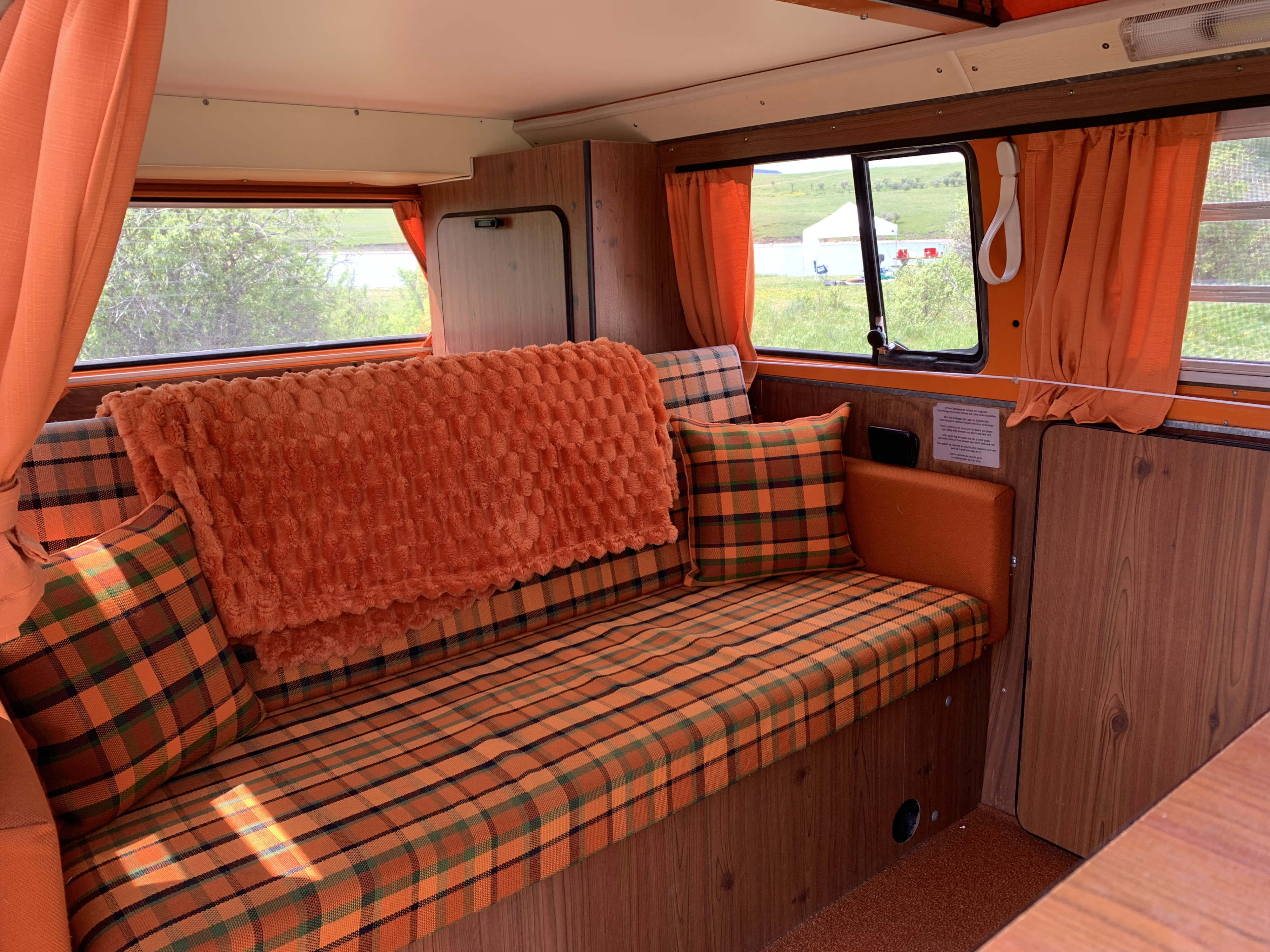Cozy vintage RV rental interior: orange plaid seating, comfy throw blanket, and wood paneling.. Volkswagen Kombi T2 Westfalia 1974