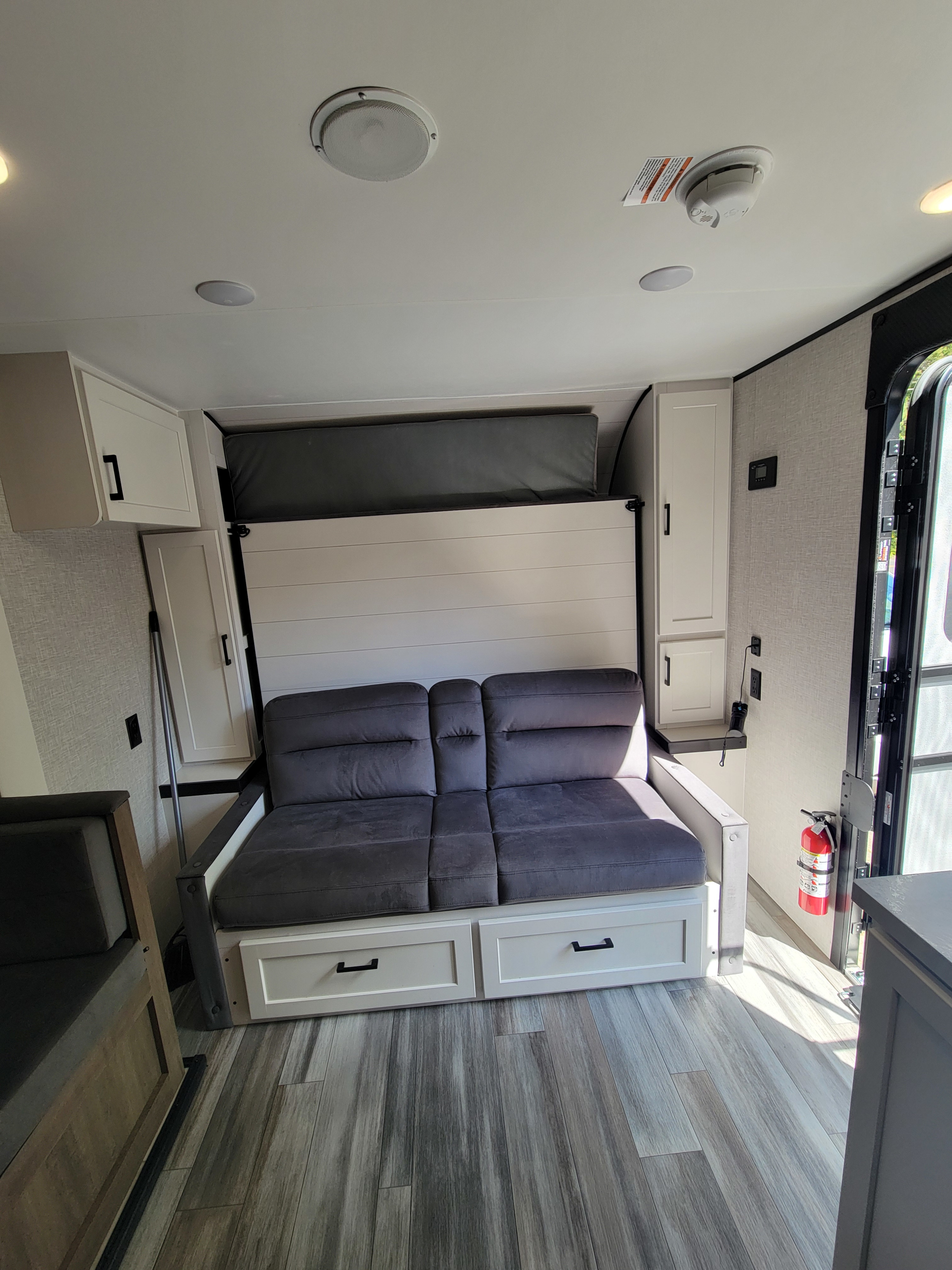 RV rental's modern living space features a gray sofa, pull-down murphy bed, white cabinetry, and wood-look floor.. Jayco Jay Flight SLX 197MBW Baja Edition 2025