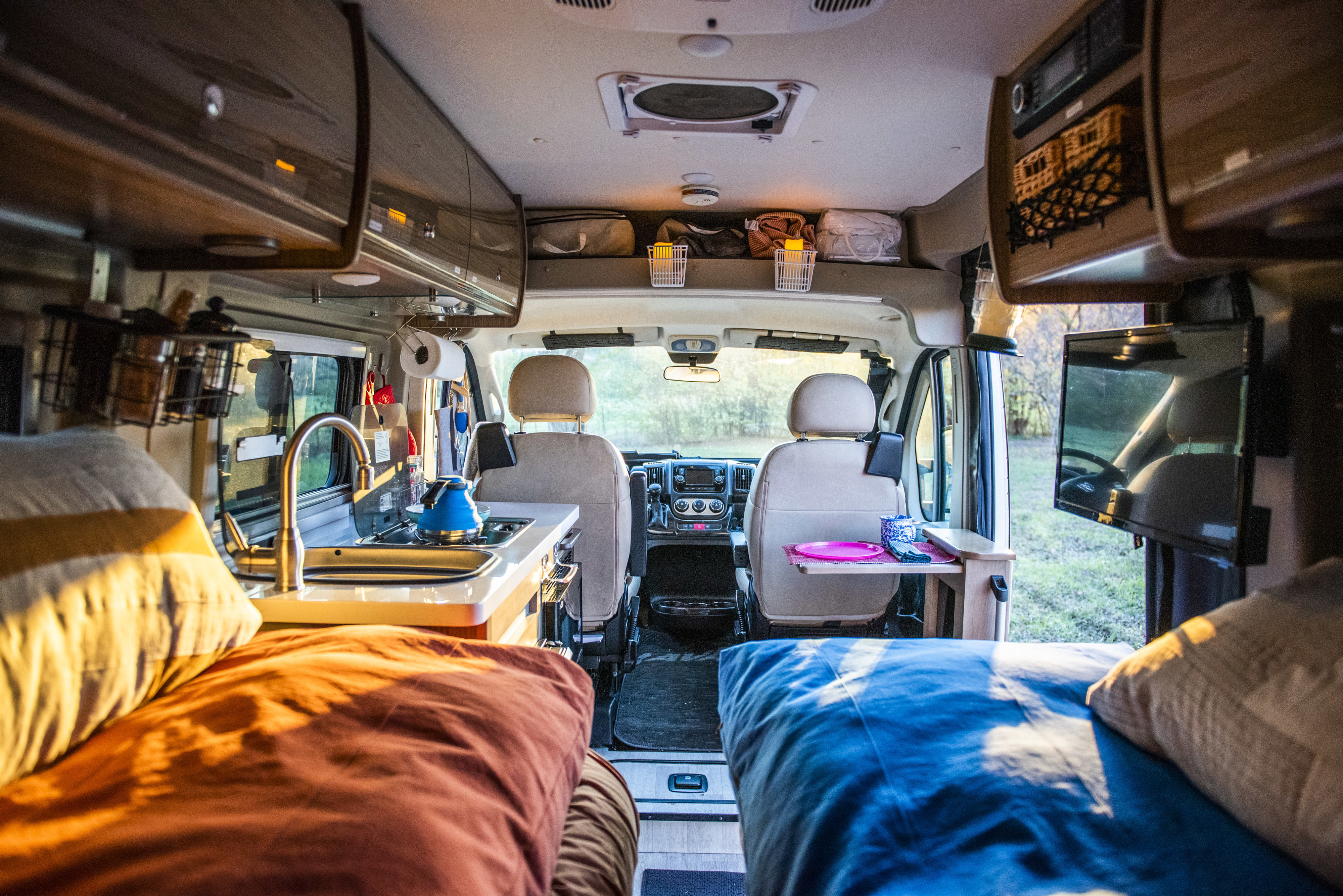 Cozy RV rental interior with kitchen, sleeping areas, and the front cabin view towards nature.. Winnebago Travato 2020