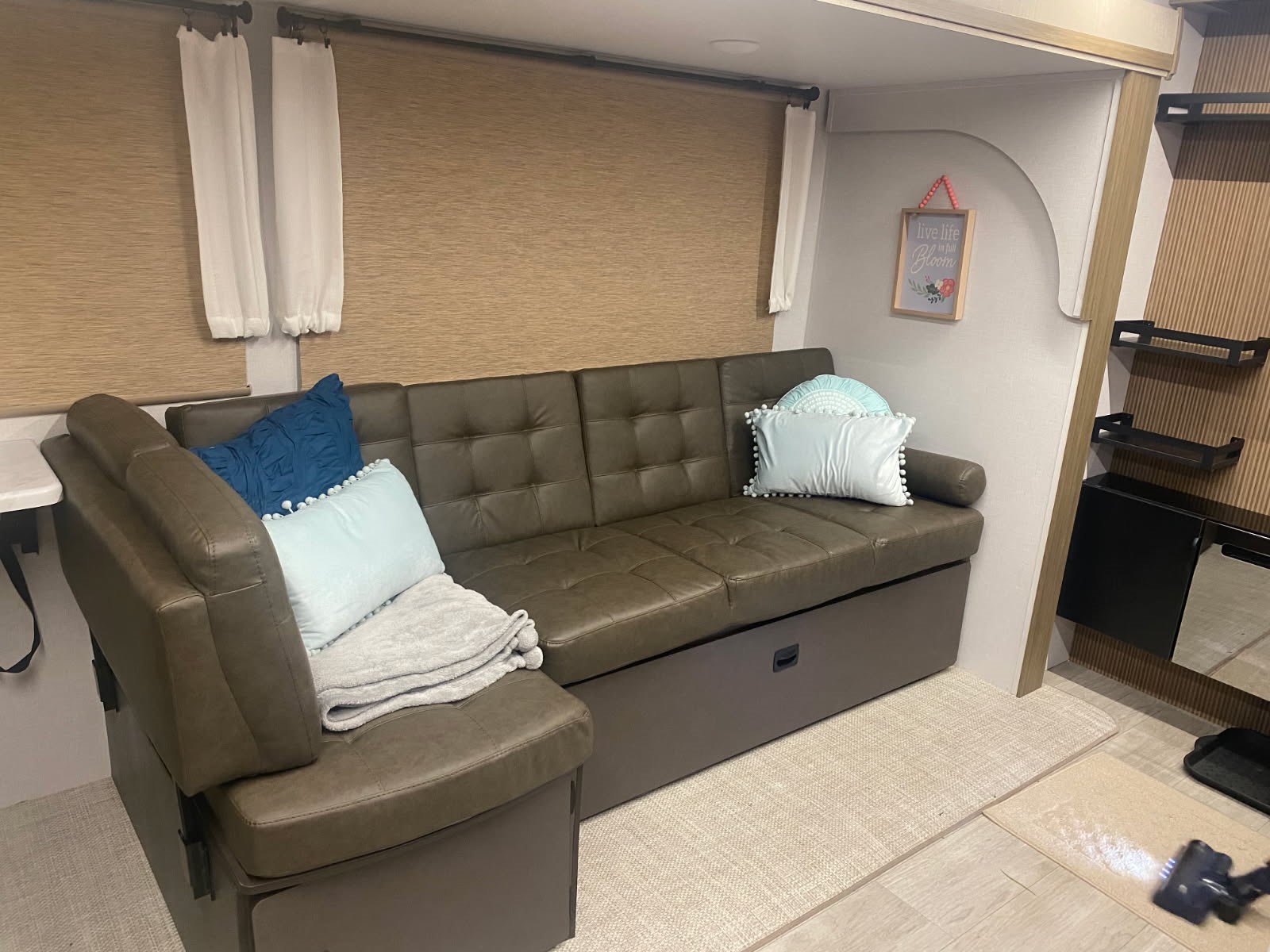 Cozy RV rental living area: brown sectional sofa with pillows, light blinds, & decor. Floor being vacuumed.. Forest River Wildwood 2025