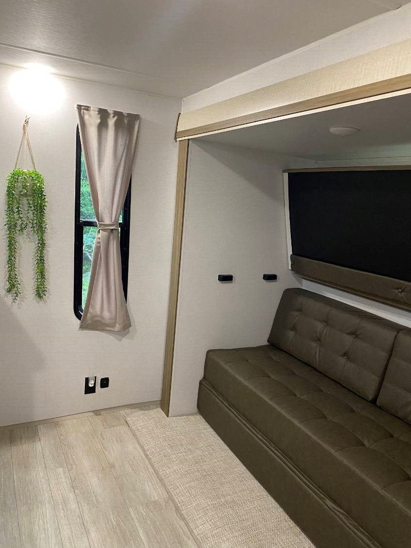 This RV rental's bright interior features a modern living space with a tufted sofa, window, and a hanging plant by the light.. Forest River Wildwood 2025