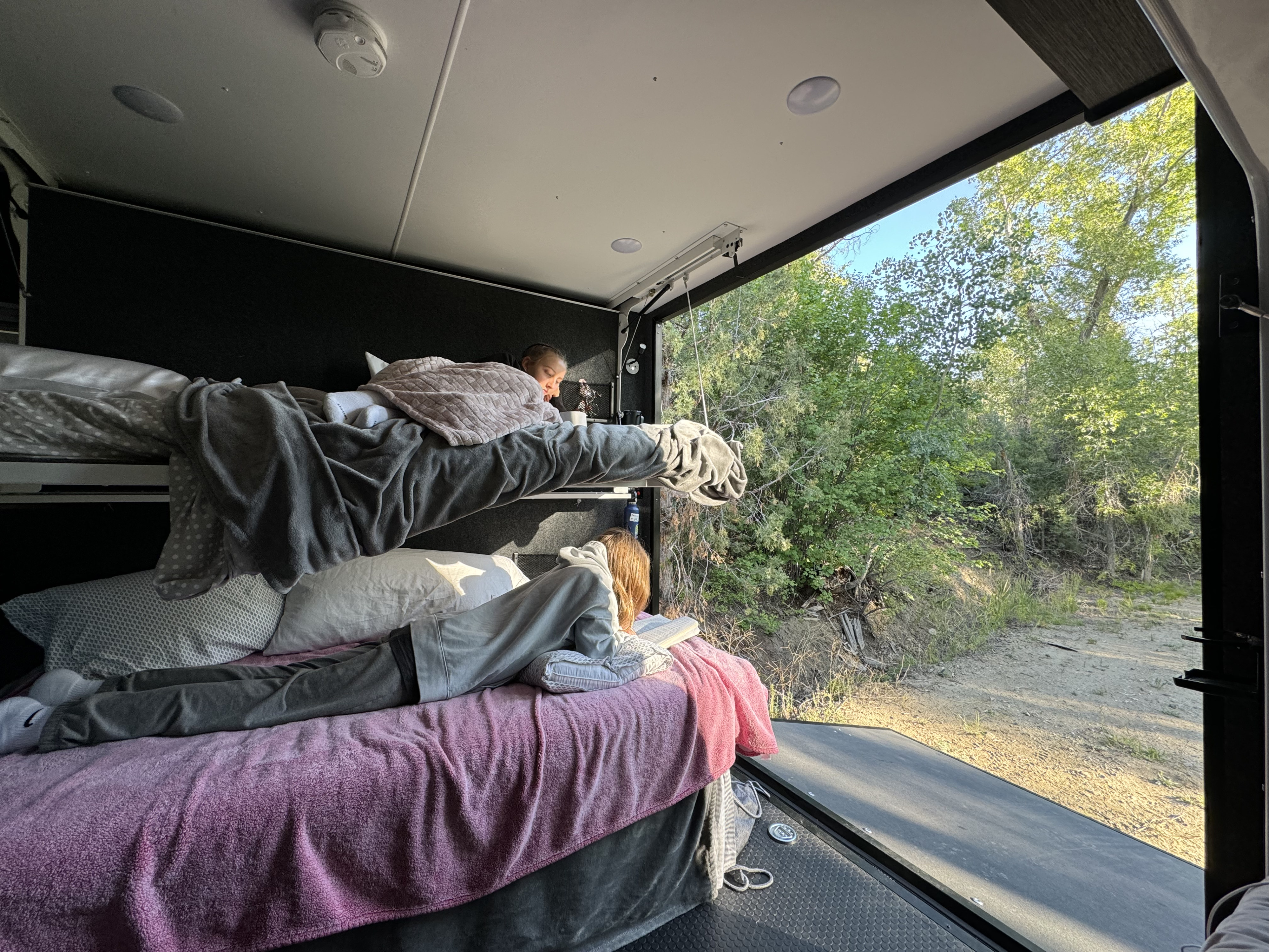Kids relax on bunk beds inside an **RV rental**, enjoying nature's view from the open back. Perfect for family adventures.. InTech RV Forge 2024