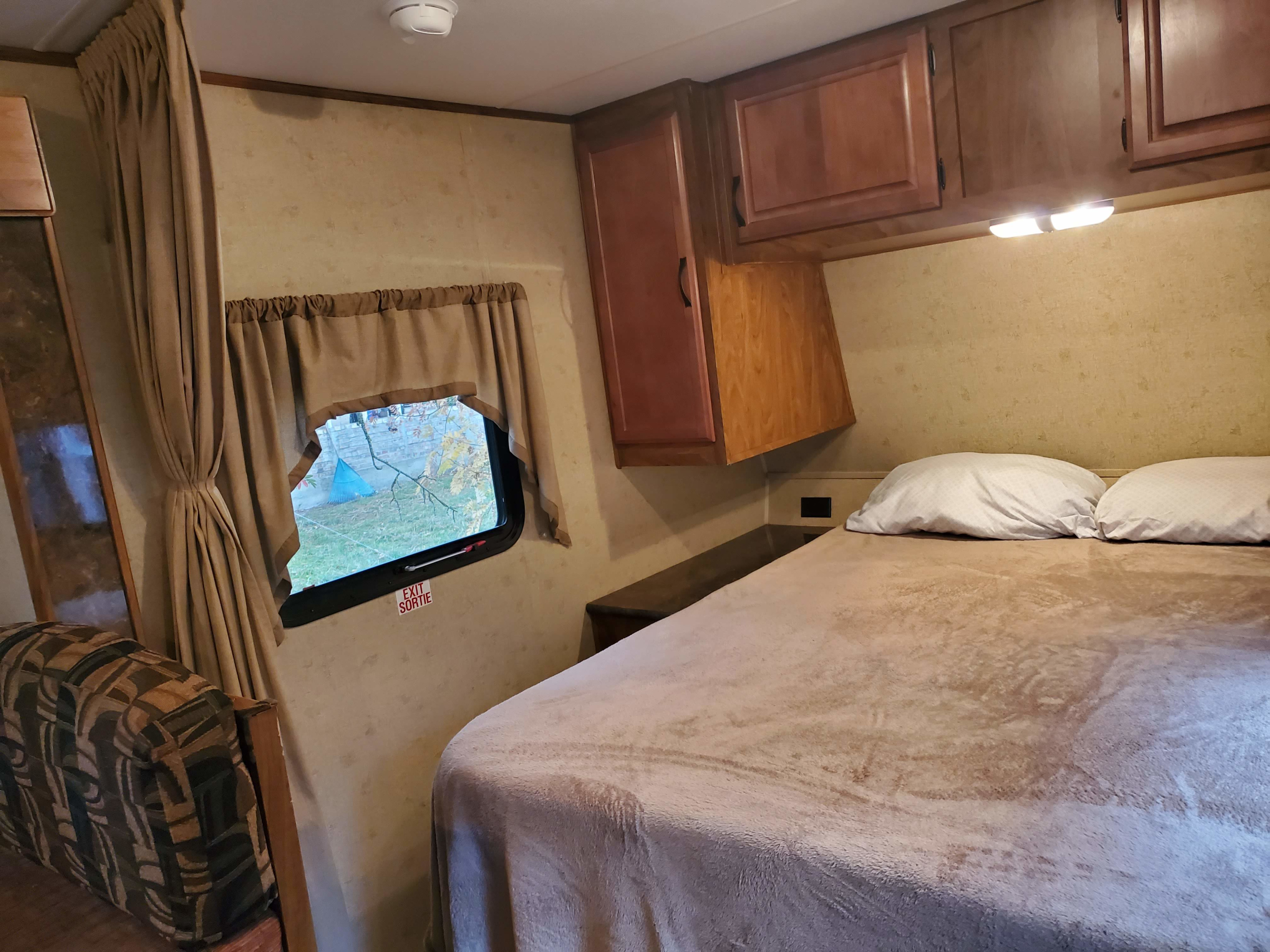 Cozy RV rental bedroom interior: comfortable bed, overhead cabinets, and a window view for relaxing travels.. Black Rock Black Rock Trailer 2015