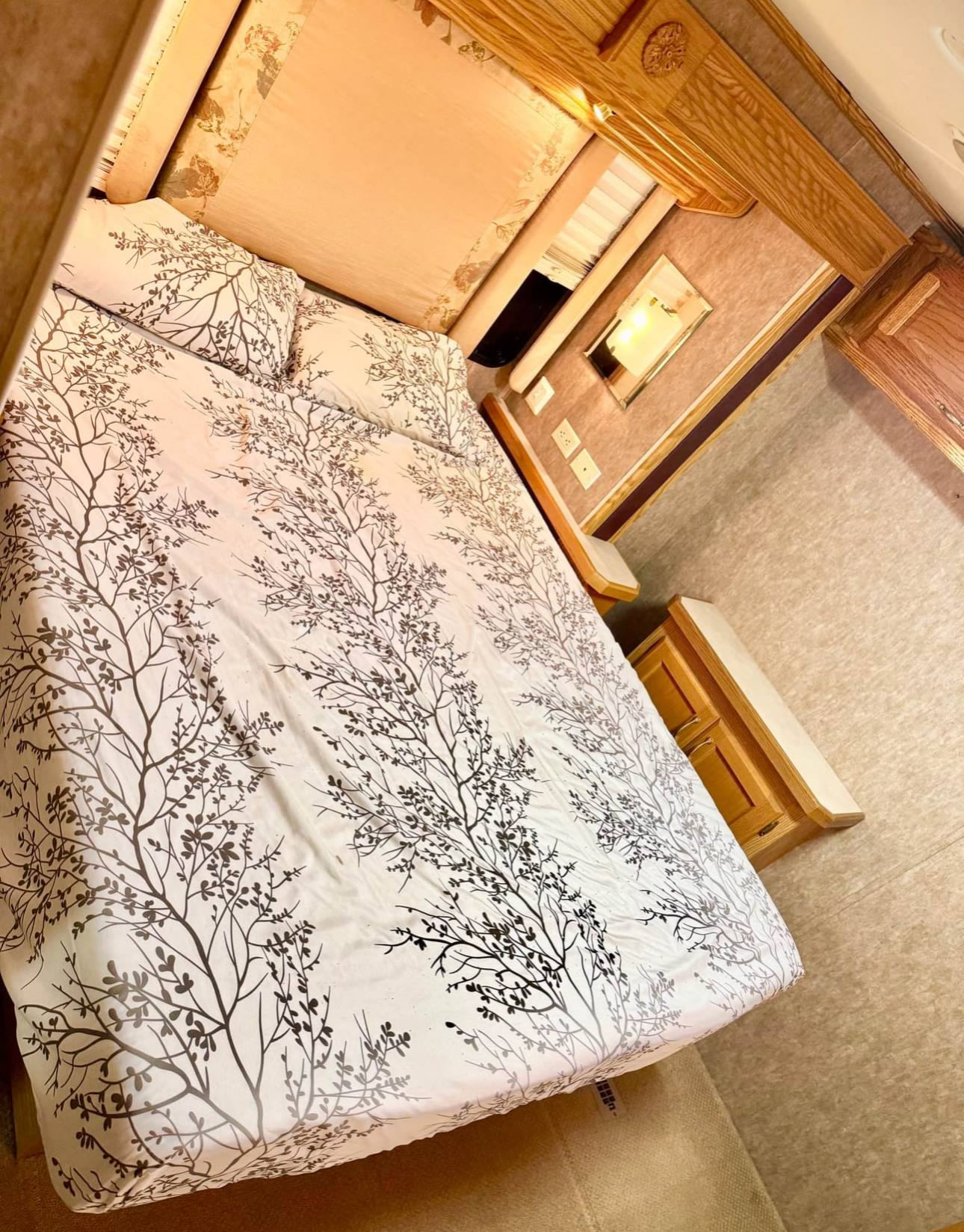 Cozy RV bedroom with tree-patterned bedding and wooden cabinets, perfect for your next RV rental.. Holiday Rambler Admiral SE 2005