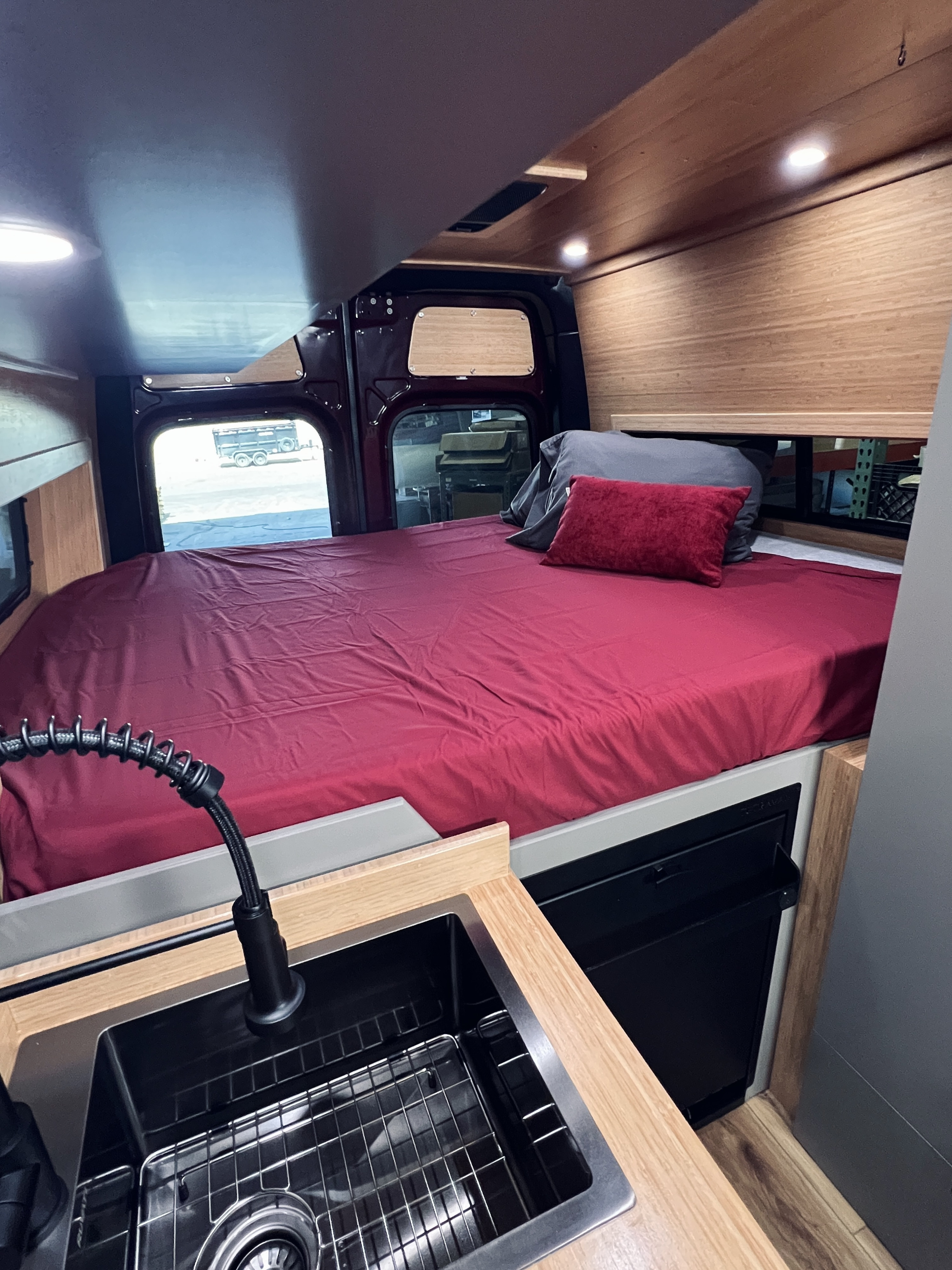 Spacious RV rental interior featuring a comfy bed, modern sink, wood accents, and ample light.. Mercedes-Benz Sprinter 2025