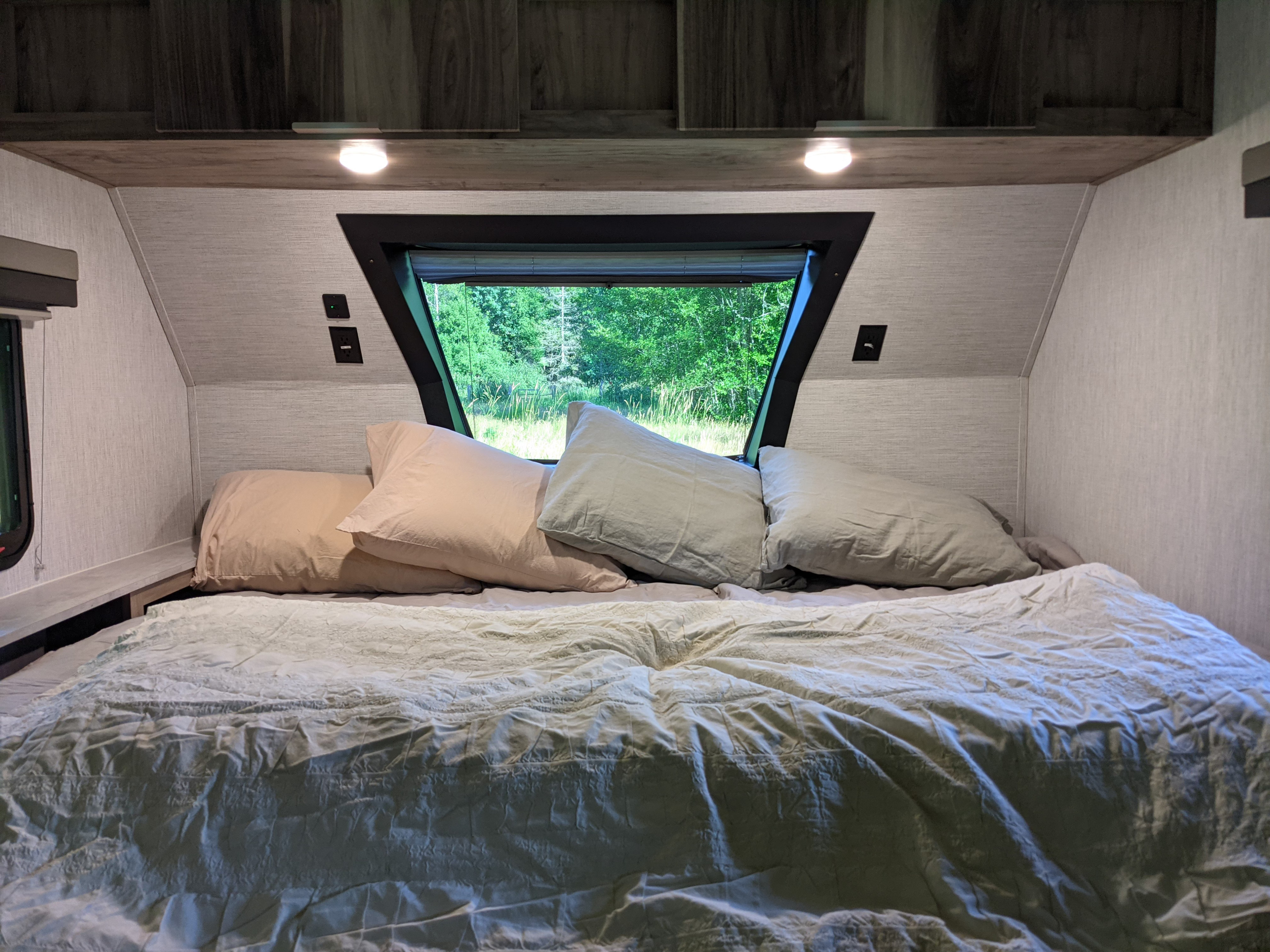 Cozy RV rental bedroom with a large bed, pillows, and window view of lush green trees, perfect for a peaceful night.. Forest River Palomino Real-Lite Mini 2021