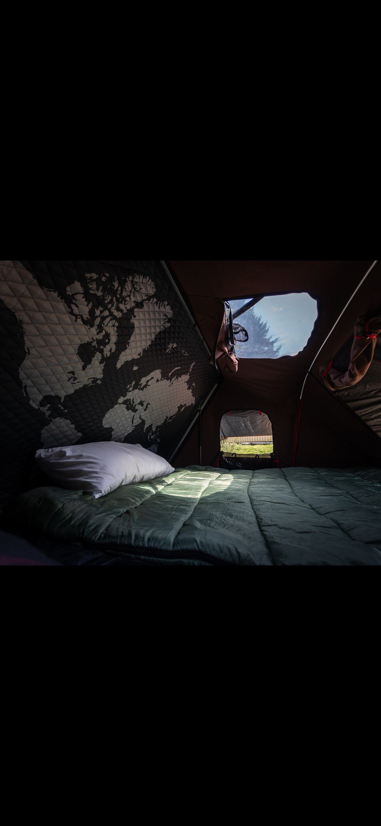 Cozy RV rental rooftop tent interior with world map, bed, and outdoor view for adventurous travelers.. Ford F350 2025