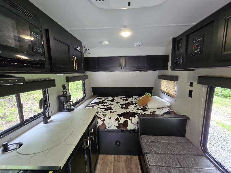 Step inside this RV rental's modern interior. Features a compact kitchen, comfy cow-print bed, and cozy seating area. Ideal for travel.. Forest River Cherokee Wolf Pup 2021