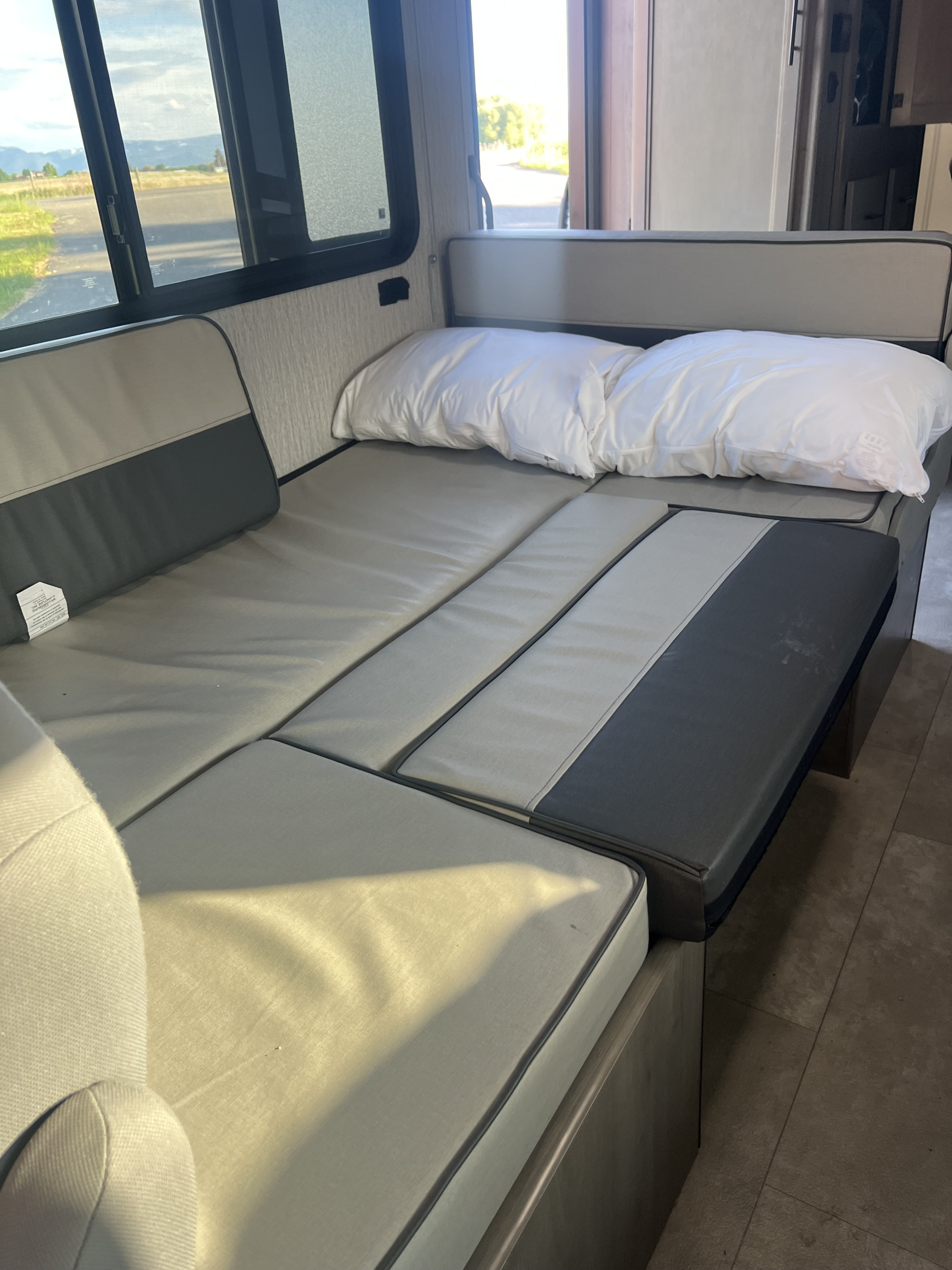 RV rental interior featuring a cozy dinette seating area transformed into a bed with pillows, next to large windows.. Coachmen RV Freelander 26DS 2023