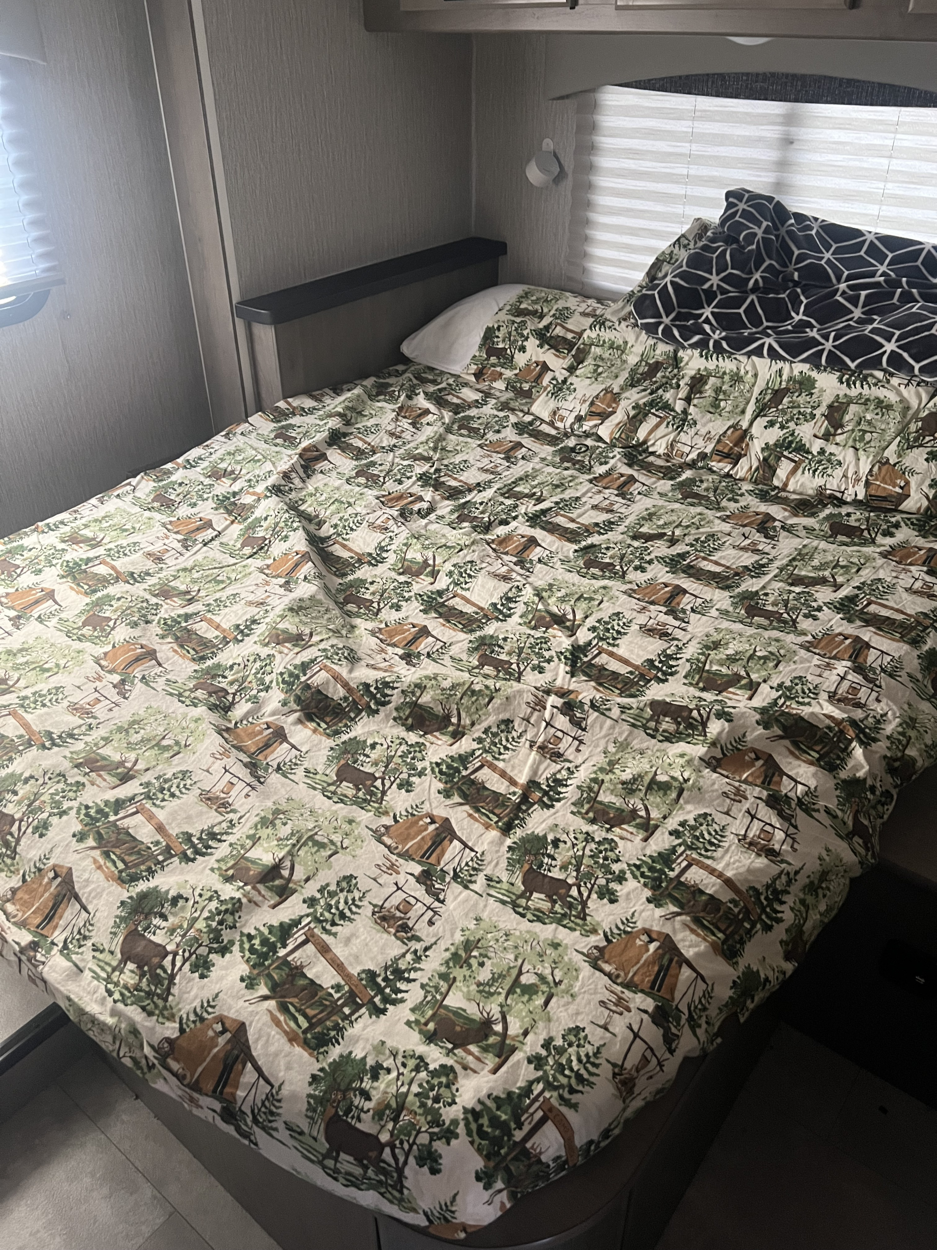 This cozy RV rental features a bed with a nature-themed comforter showing deer and tents, ideal for camping adventures.. Coachmen RV Freelander 26DS 2023