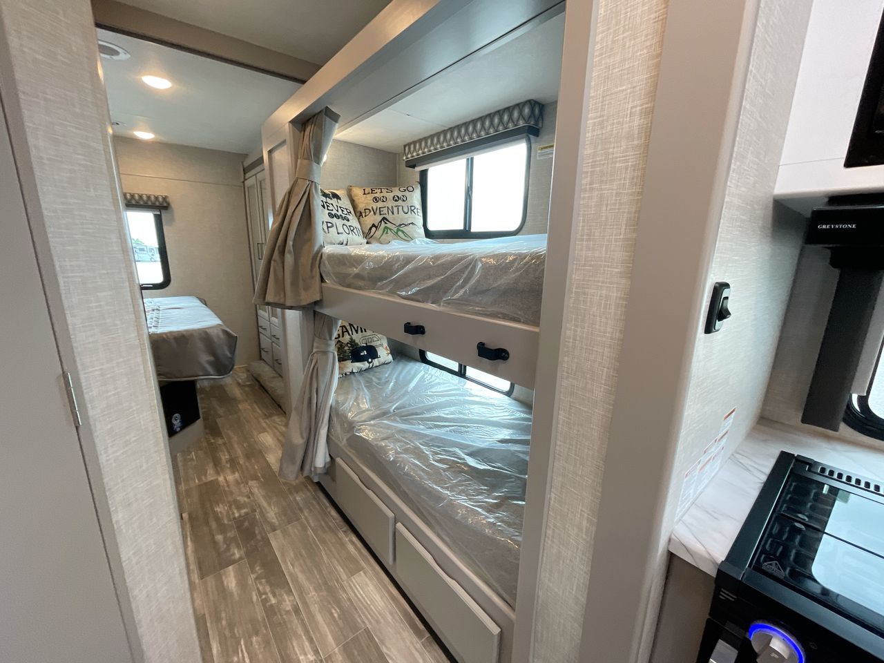 Inside an RV rental featuring compact bunk beds with plastic wrap, a kitchen area, and a rear bed. Ideal for road trips.. Thor Geneva 2024