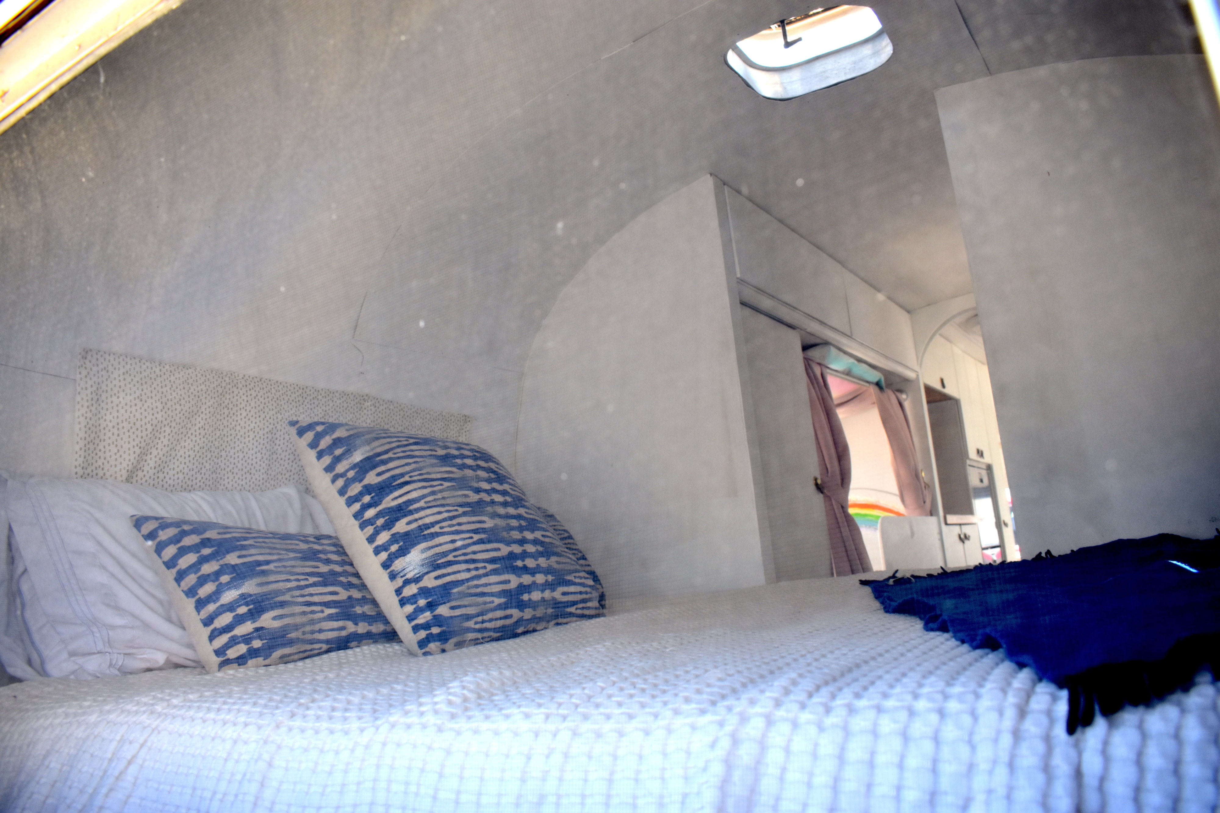 Cozy RV rental bedroom featuring white bedding, blue patterned pillows, and a curved ceiling with a skylight.. Airstream Sovereign 1974