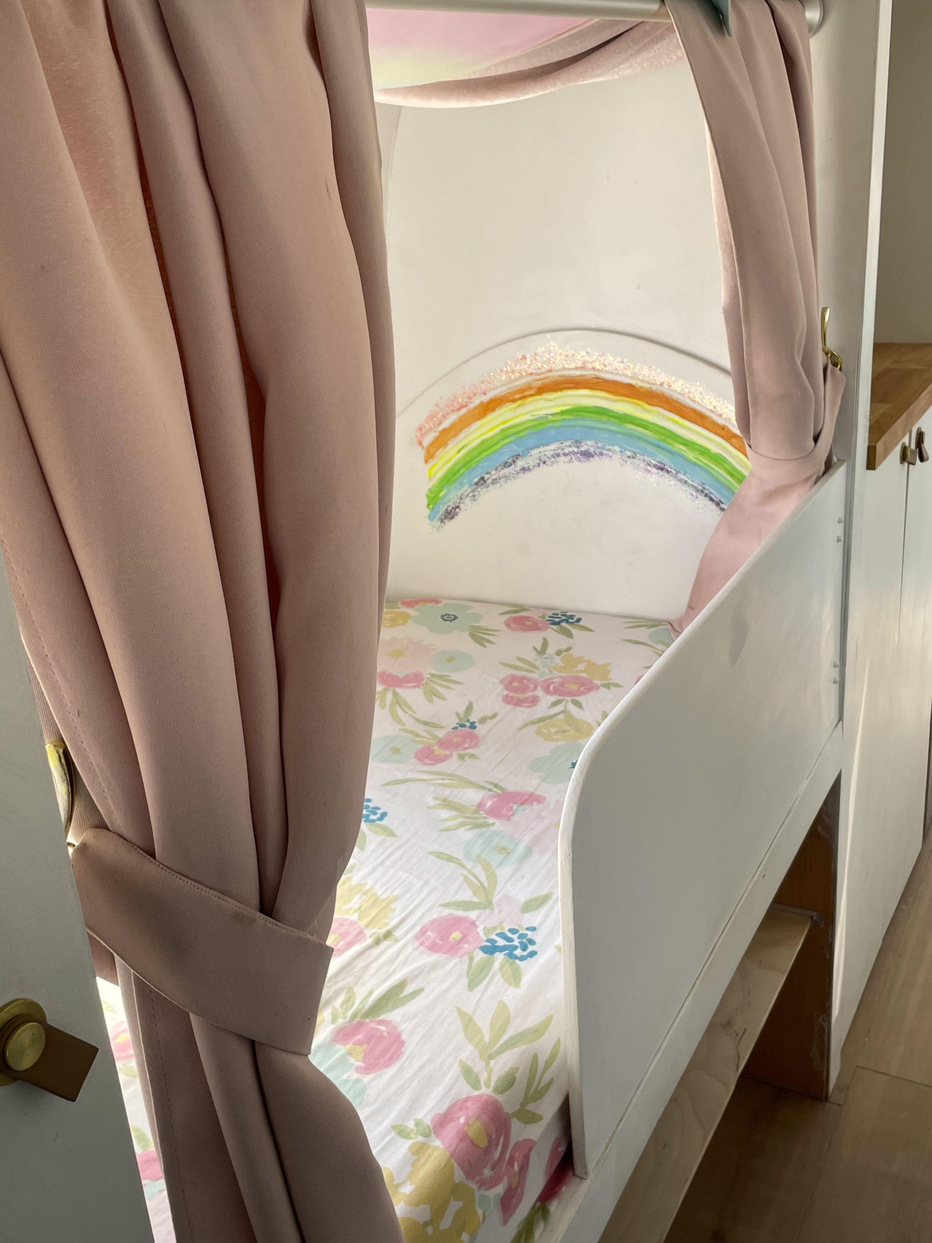 Sweet RV rental interior: A child's built-in bed with pink curtains, a rainbow mural, and floral bedding.. Airstream Sovereign 1974
