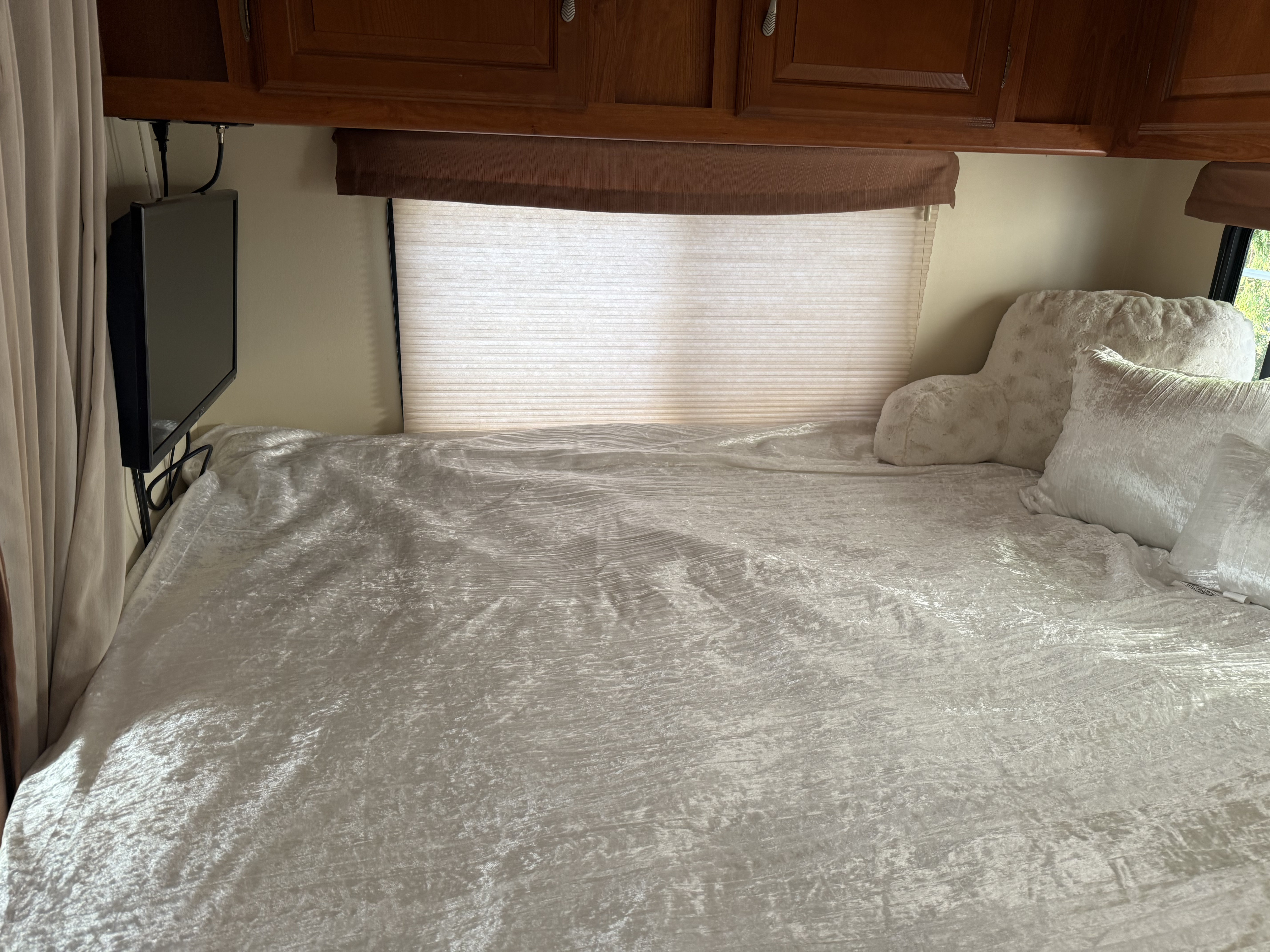 Inside an RV rental: a compact bedroom featuring a bed with velvet bedding, overhead cabinets, and a mounted TV.. Coachmen Freelander 2008