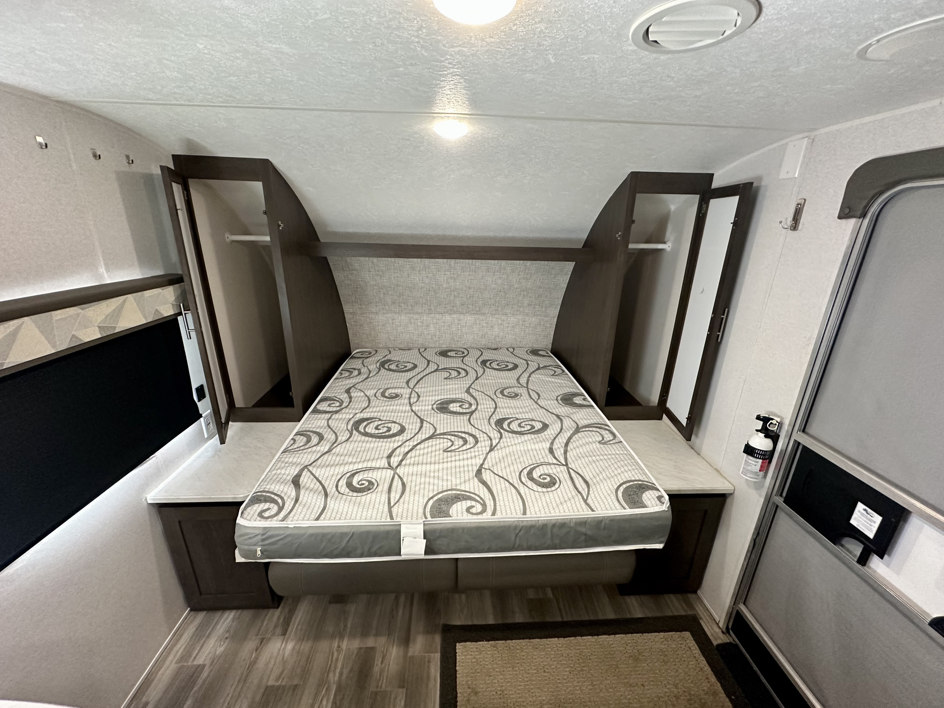 RV rental bedroom: patterned bed, dark wood cabinets, side counters, and overhead storage for a functional space.. Forest River Wildwood X-Lite 2020