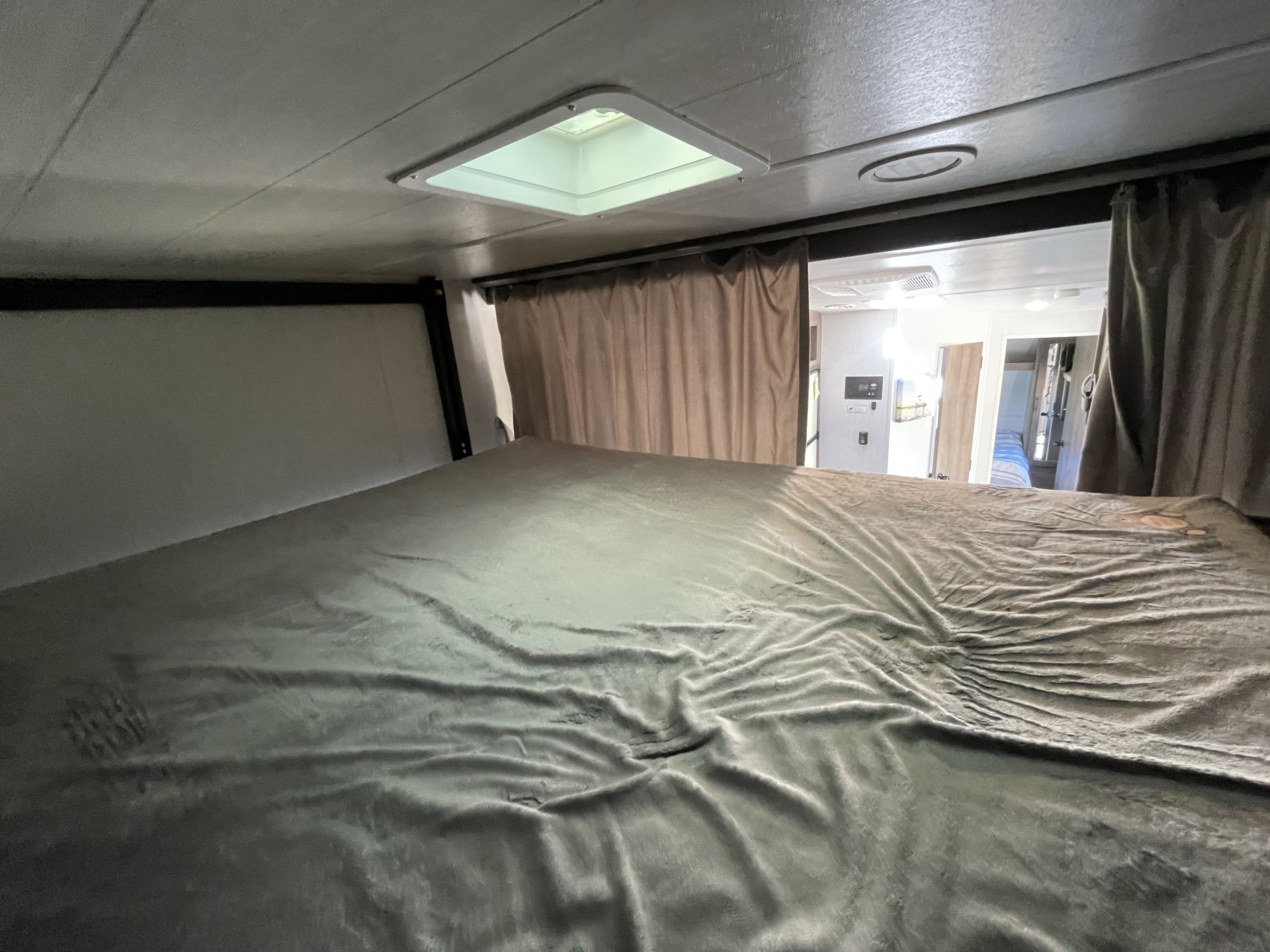 Spacious rv rental bunk bed with grey comforter & ceiling skylight. Curtains reveal glimpse of main living area.. Forest River Salem Cruise Lite 2022