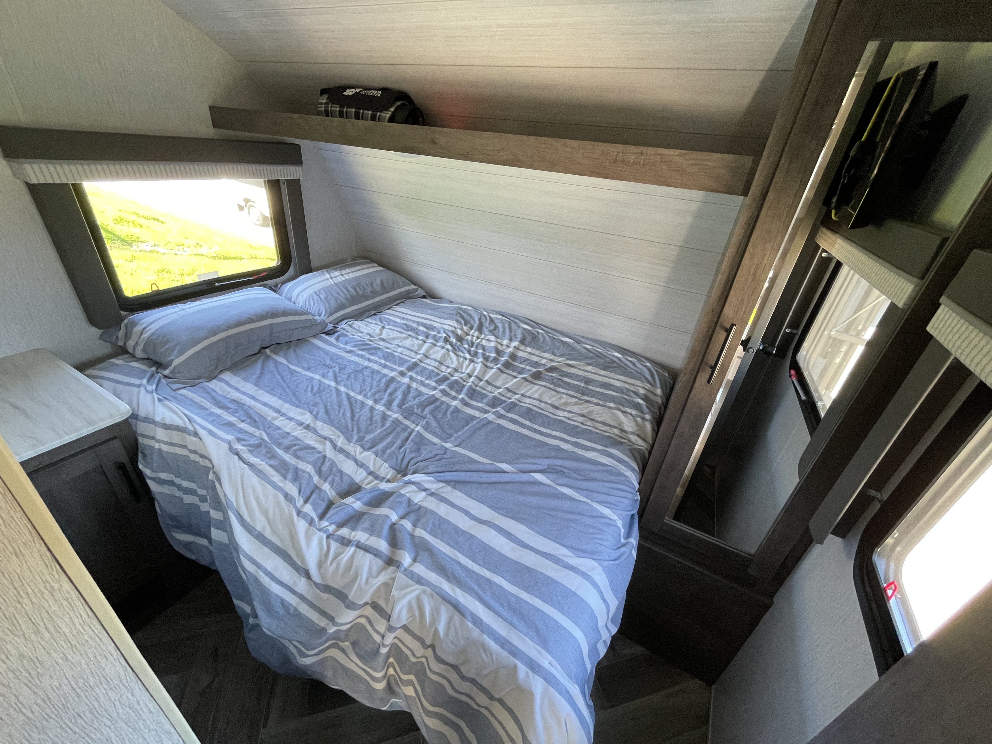 Cozy RV rental bedroom featuring a striped bed, bright window view, and built-in storage. Ideal for comfortable travel.. Forest River Salem Cruise Lite 2022